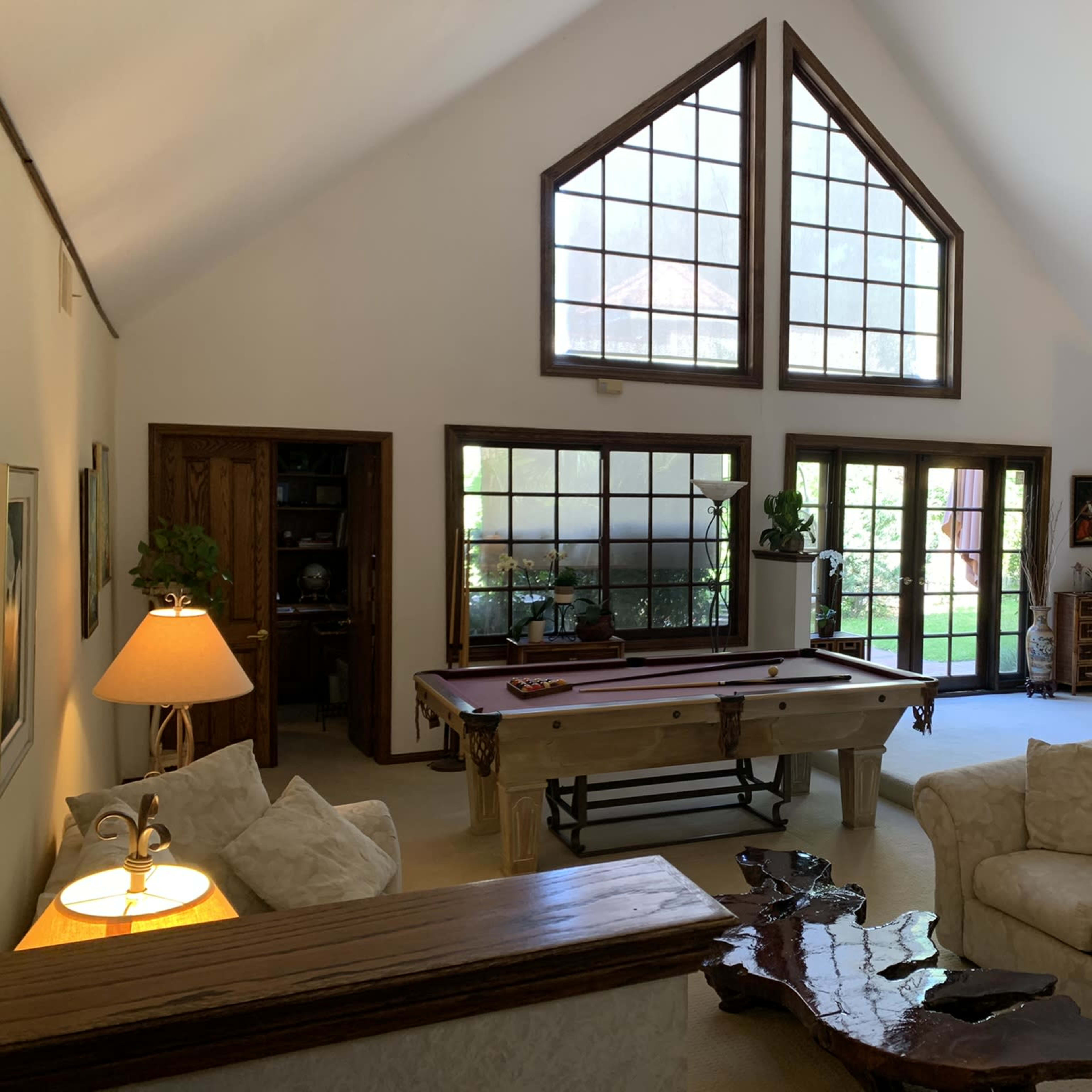 A spacious living room with a high ceiling, large windows, a pool table, and a cozy seating area.
