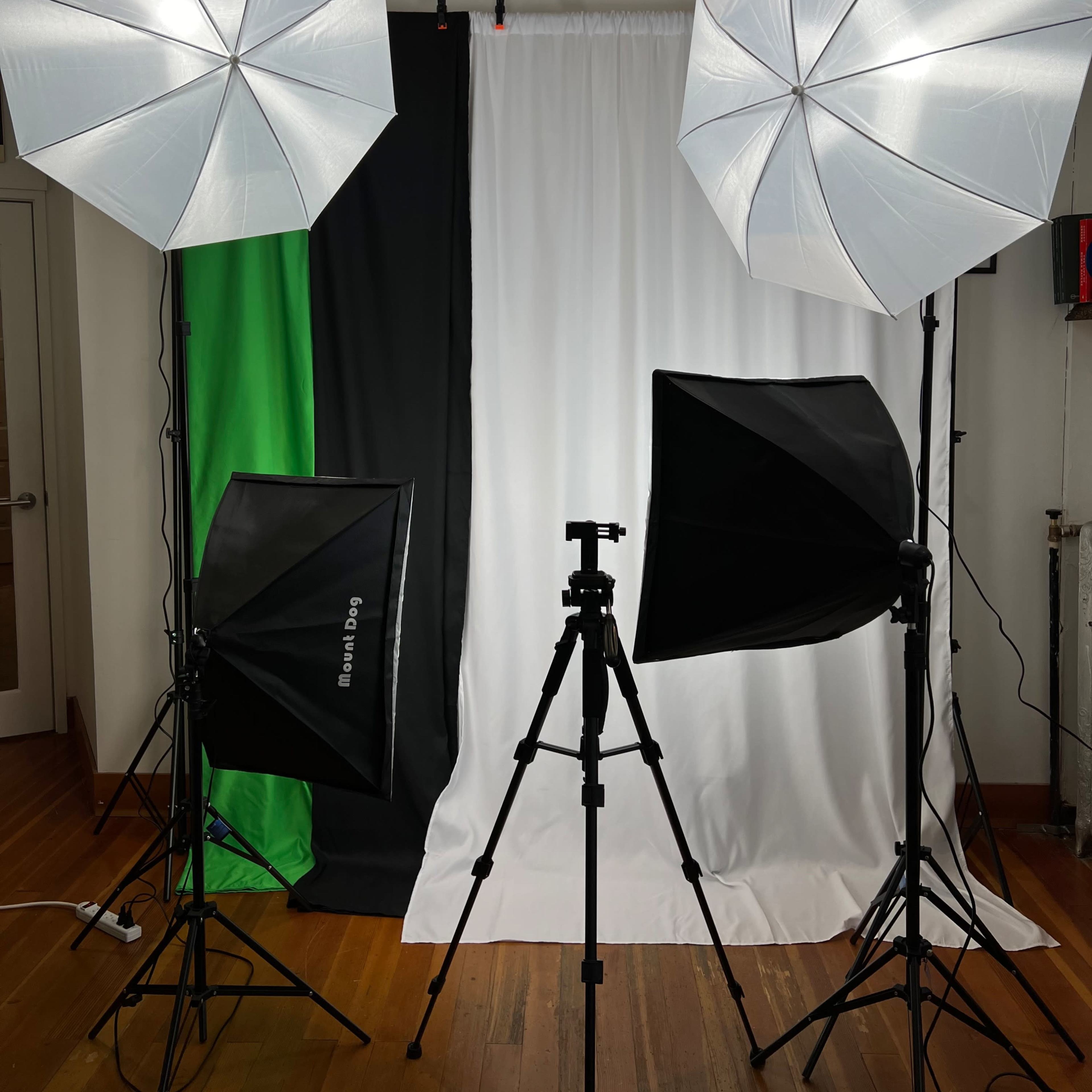 A photography setup with two large softbox lights and a smaller light on a tripod, positioned in front of a white backdrop flanked by green and black fabric.