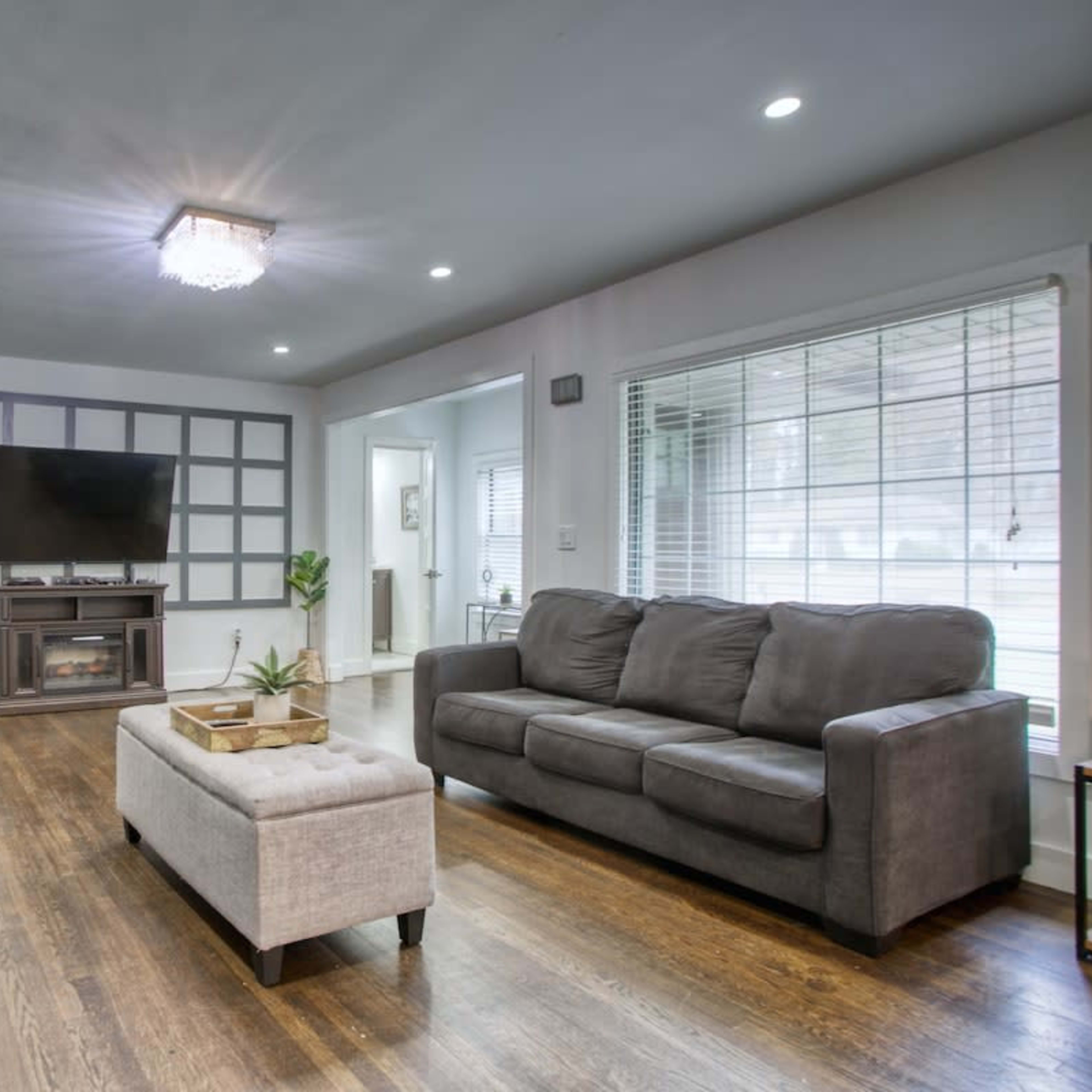 A living room with two gray sofas facing a coffee table, a television mounted on the wall, and a decorative fireplace below it.