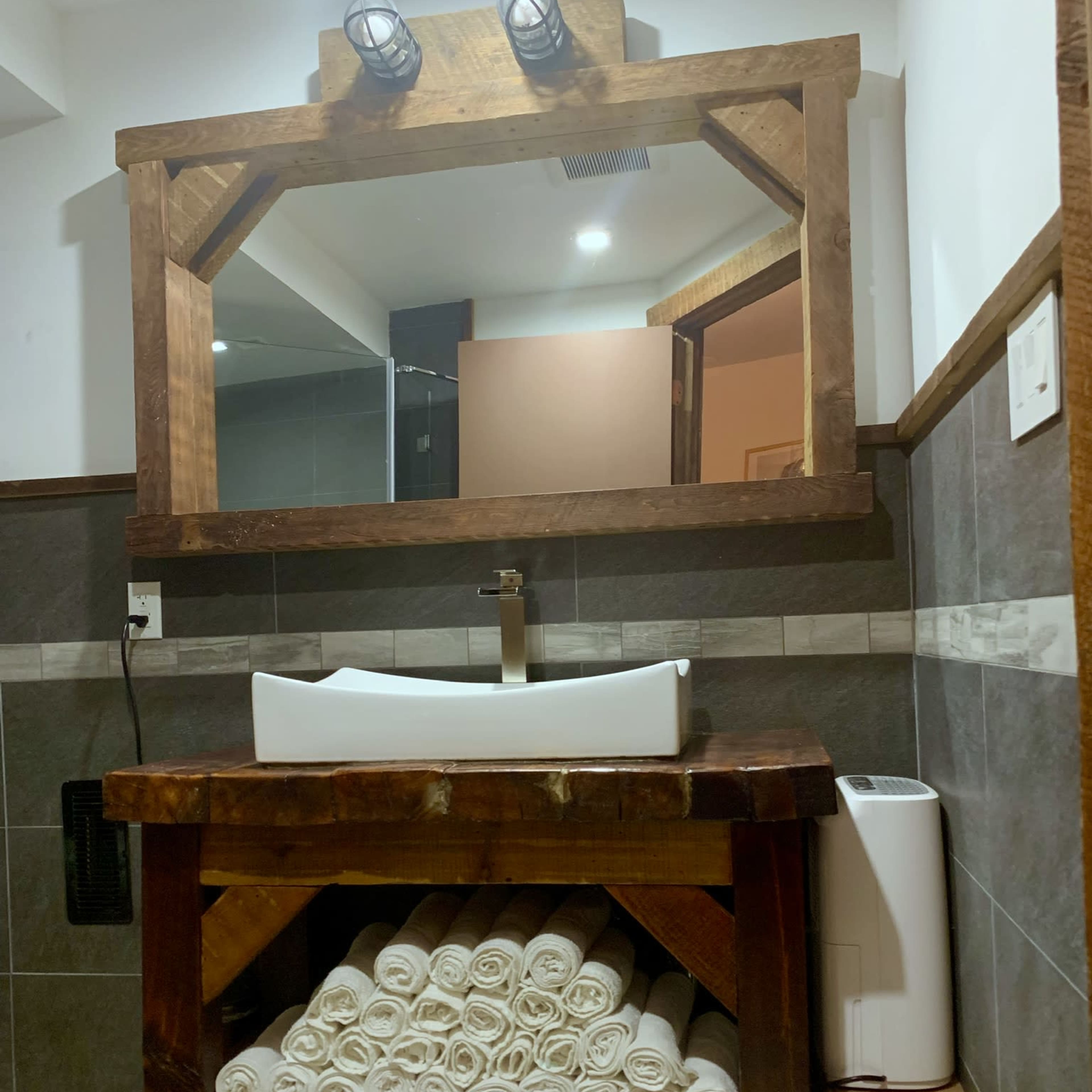 A bathroom with a wooden sink vanity, a large mirror, and neatly rolled towels stored underneath.