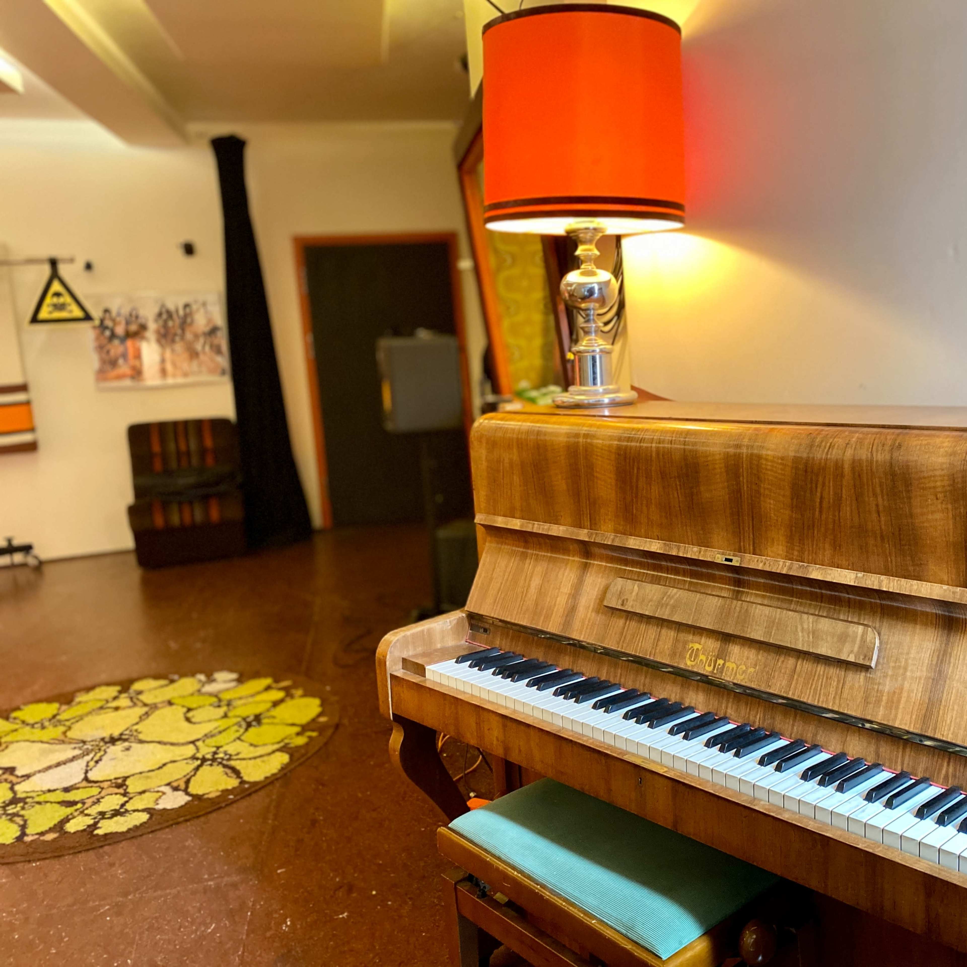 A wooden piano with a shiny lamp sits in a room that features colorful decor and patterned rugs.