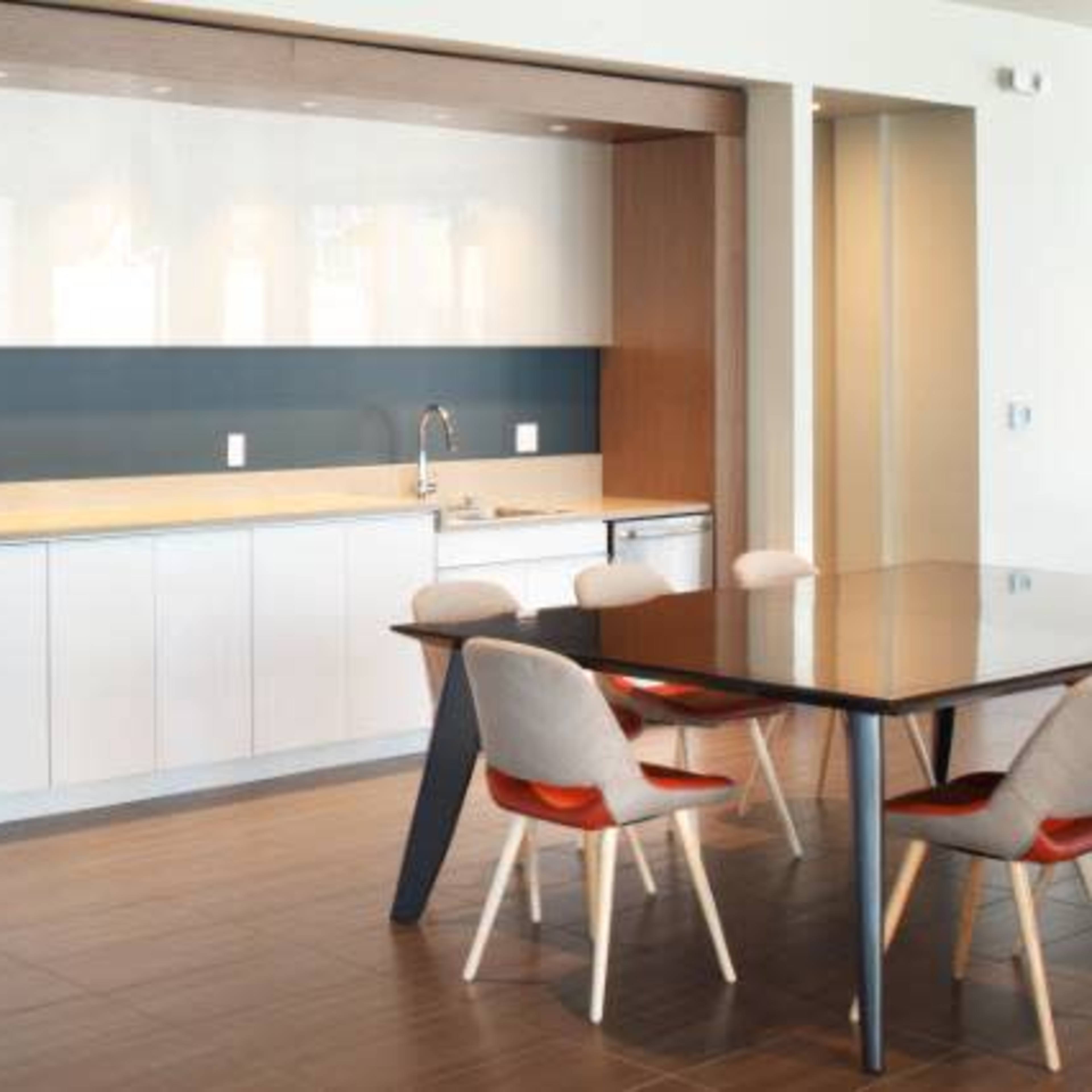 A modern kitchen area featuring a sleek white cabinetry, a dark blue accent wall, and a dining table with light-colored chairs.