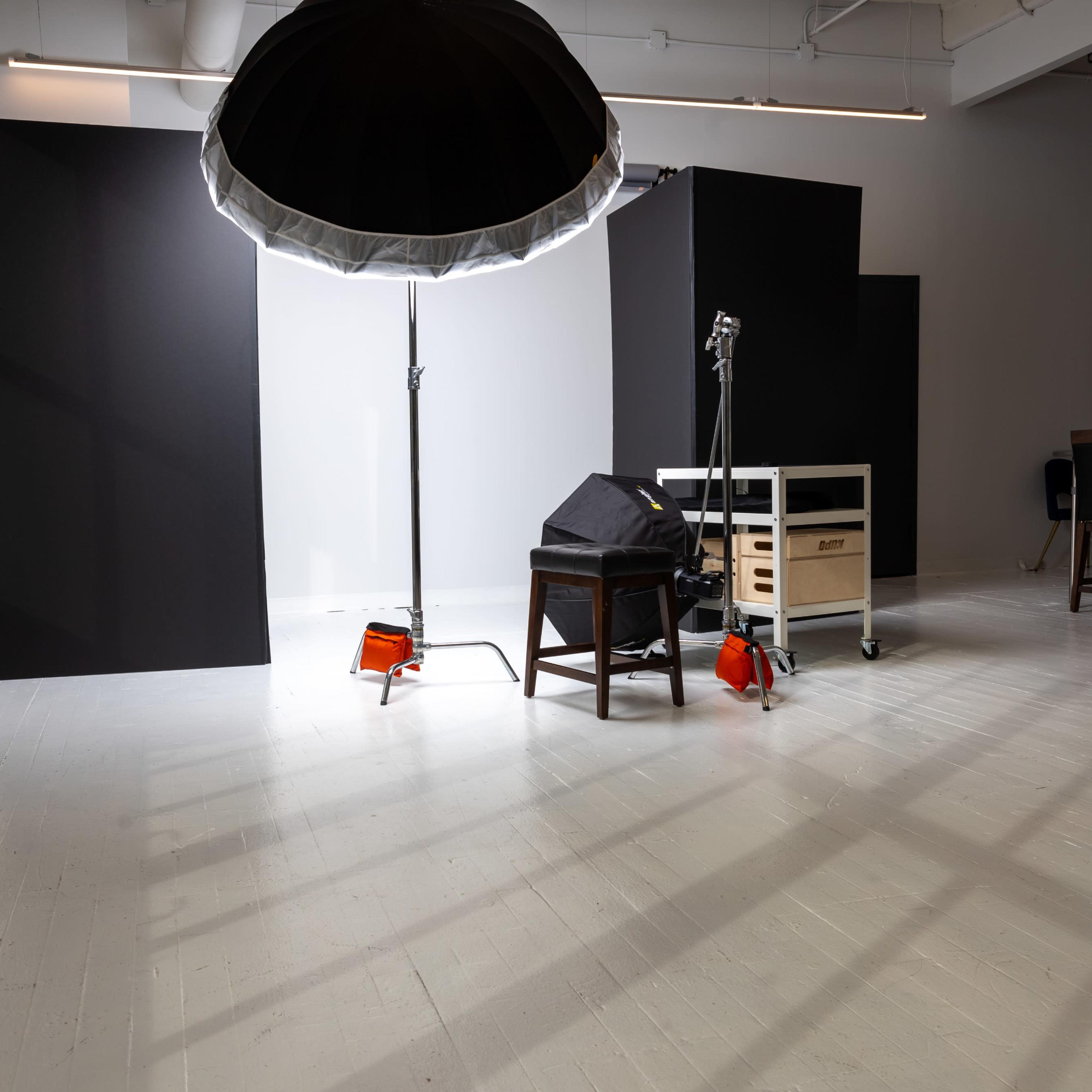 The scene shows a photography studio with a large light umbrella, backdrops, a chair, and a mobile cart.