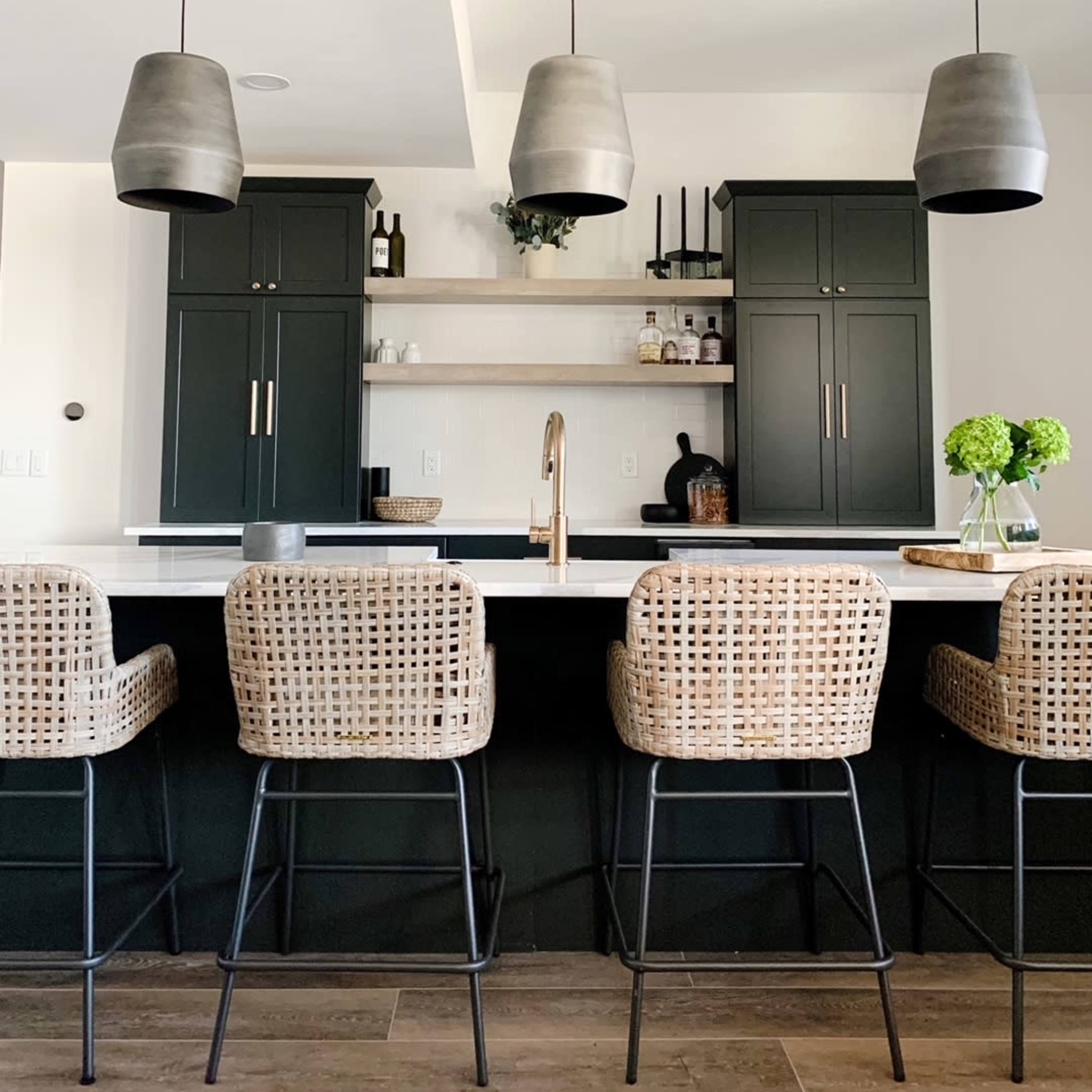 A modern kitchen features a black cabinetry backdrop, a white countertop with bar stools made of woven material, and pendant lights hanging above.