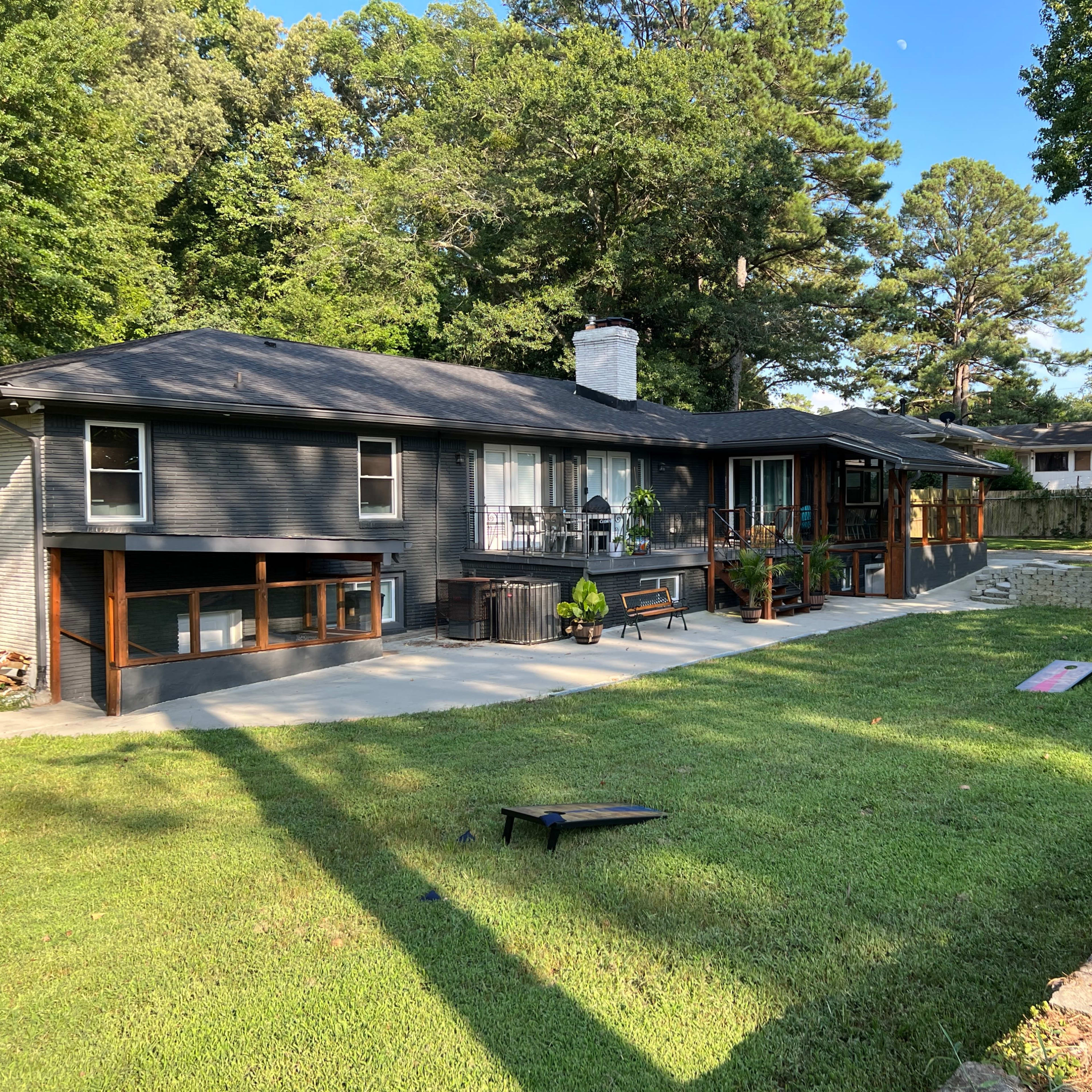A modern, single-story house with a large patio area and a well-manicured lawn surrounded by trees.