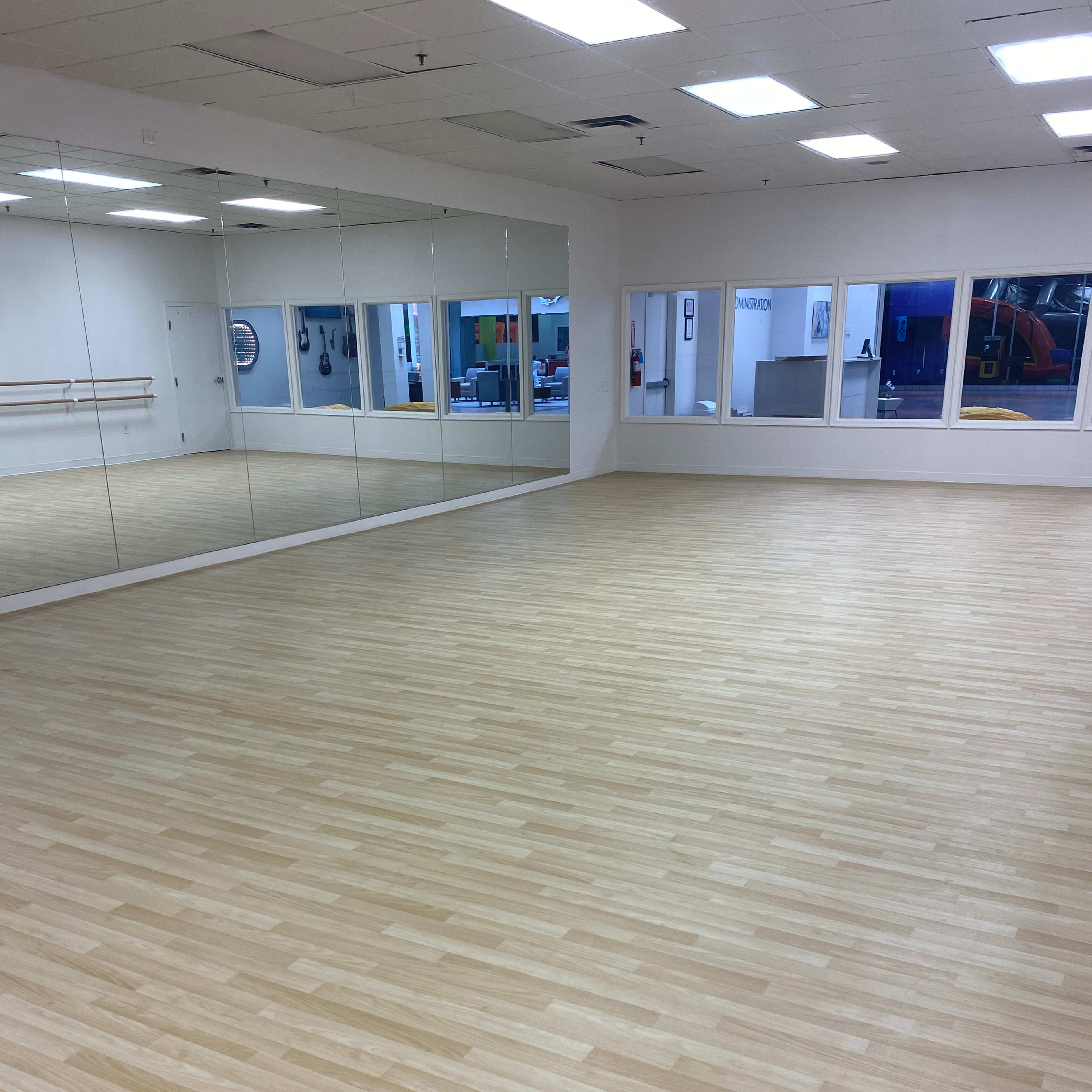 A spacious dance studio with wooden flooring and large mirrors on one wall.