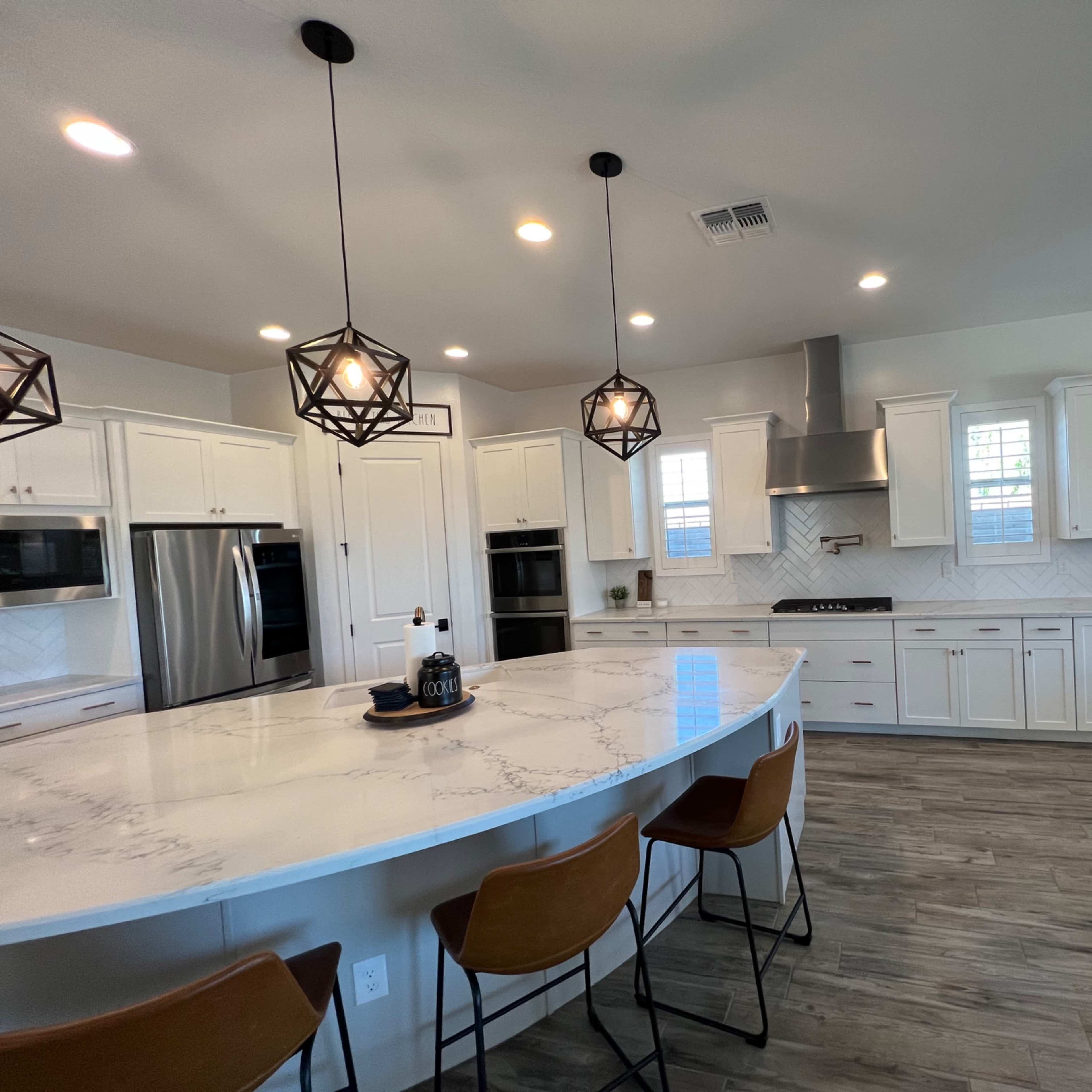 A modern kitchen features a spacious island with bar seating, stainless steel appliances, white cabinetry, and pendant lighting.
