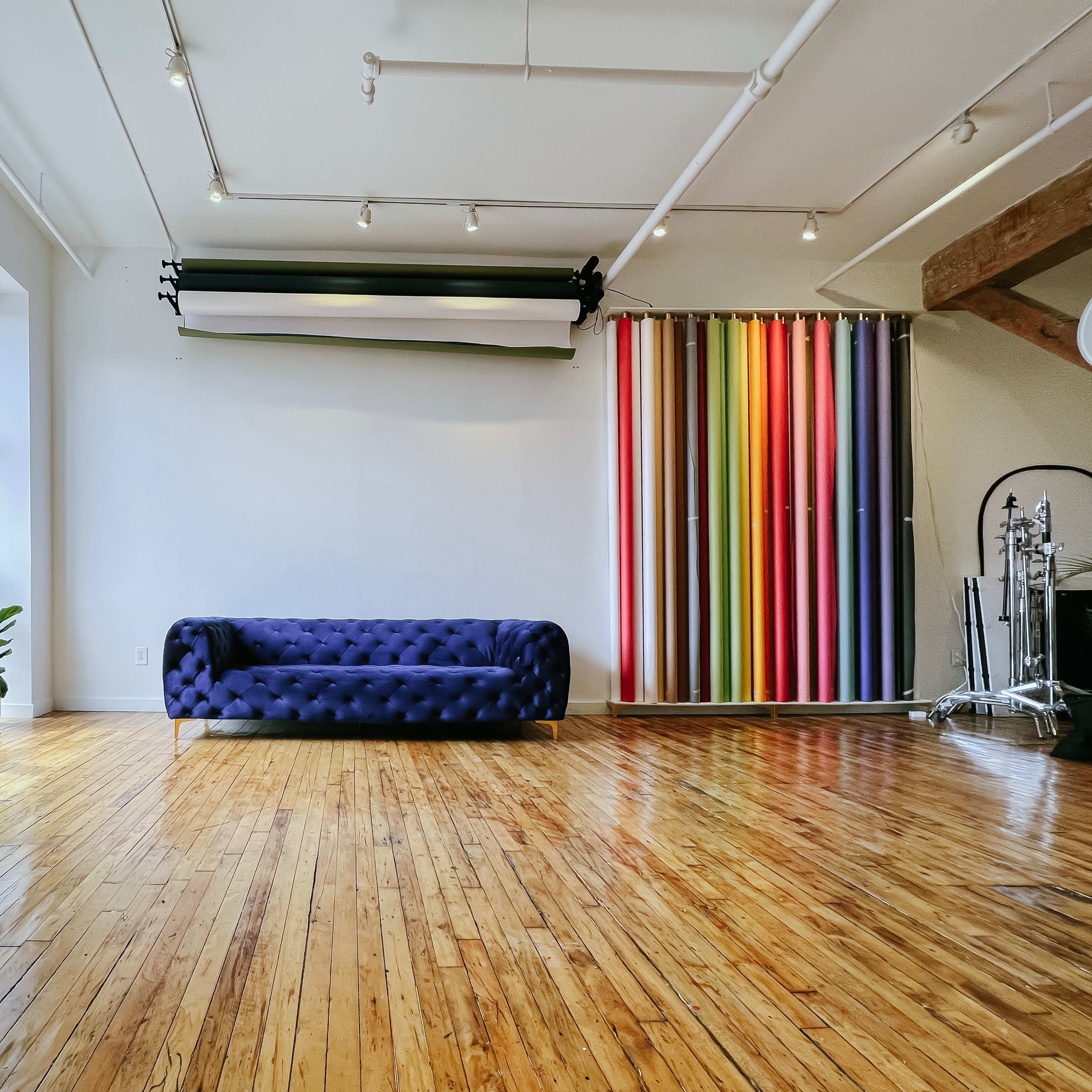 A spacious room with a blue tufted sofa placed against a wall, large windows letting in natural light, and a colorful striped backdrop on one side.