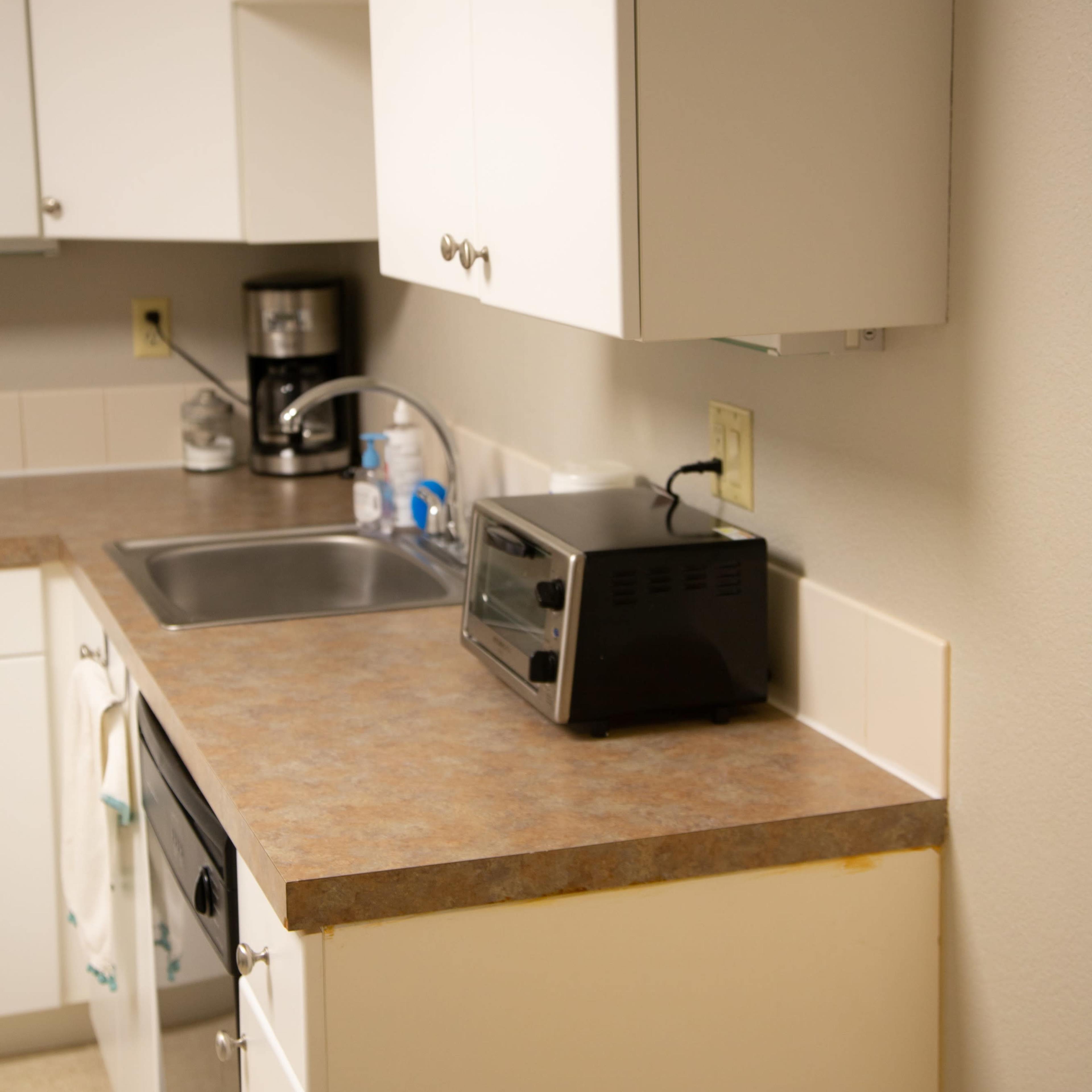 A kitchen countertop with a sink, a toaster, and a coffee maker on the shelves above.