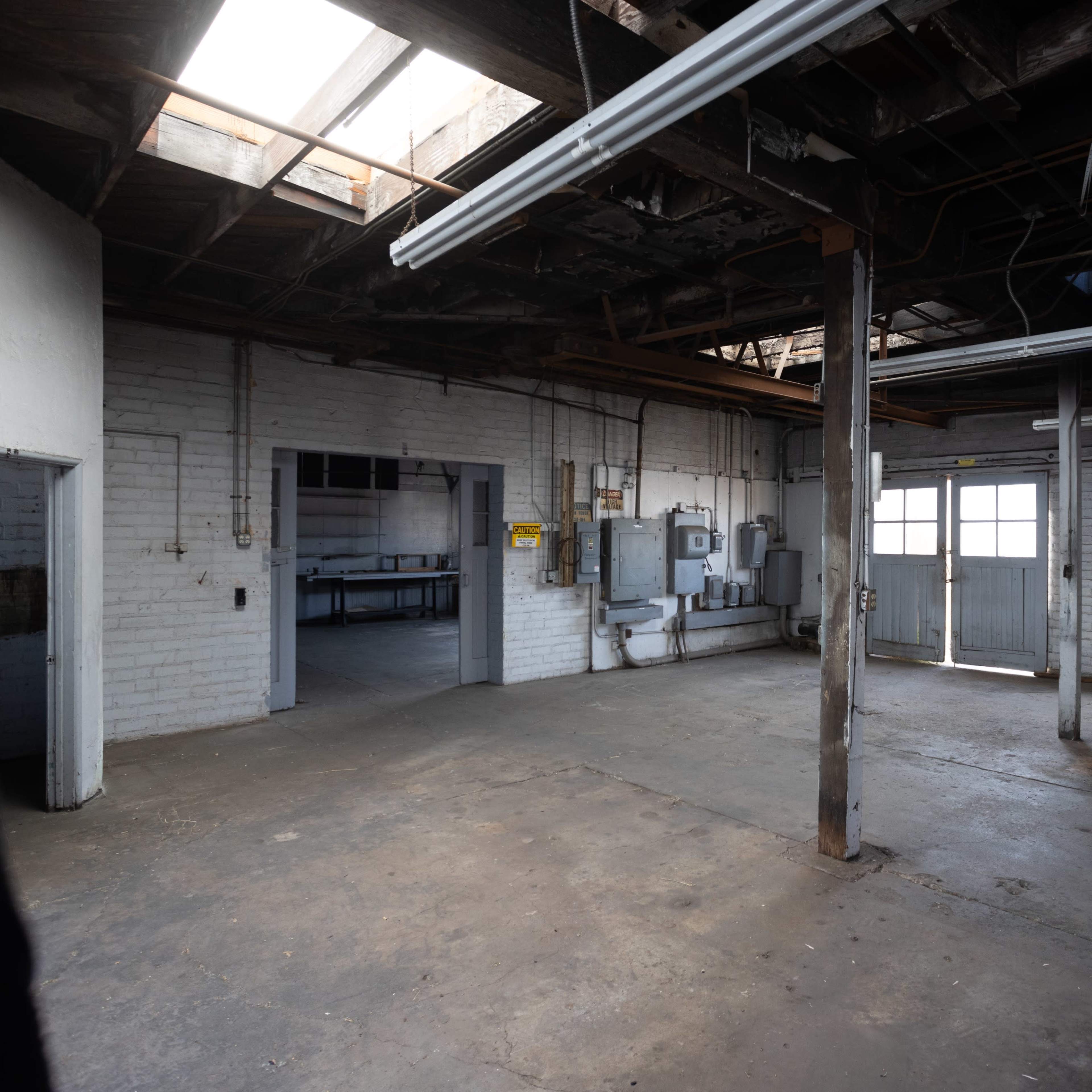 An empty industrial space with exposed beams, concrete flooring, and two entrances.