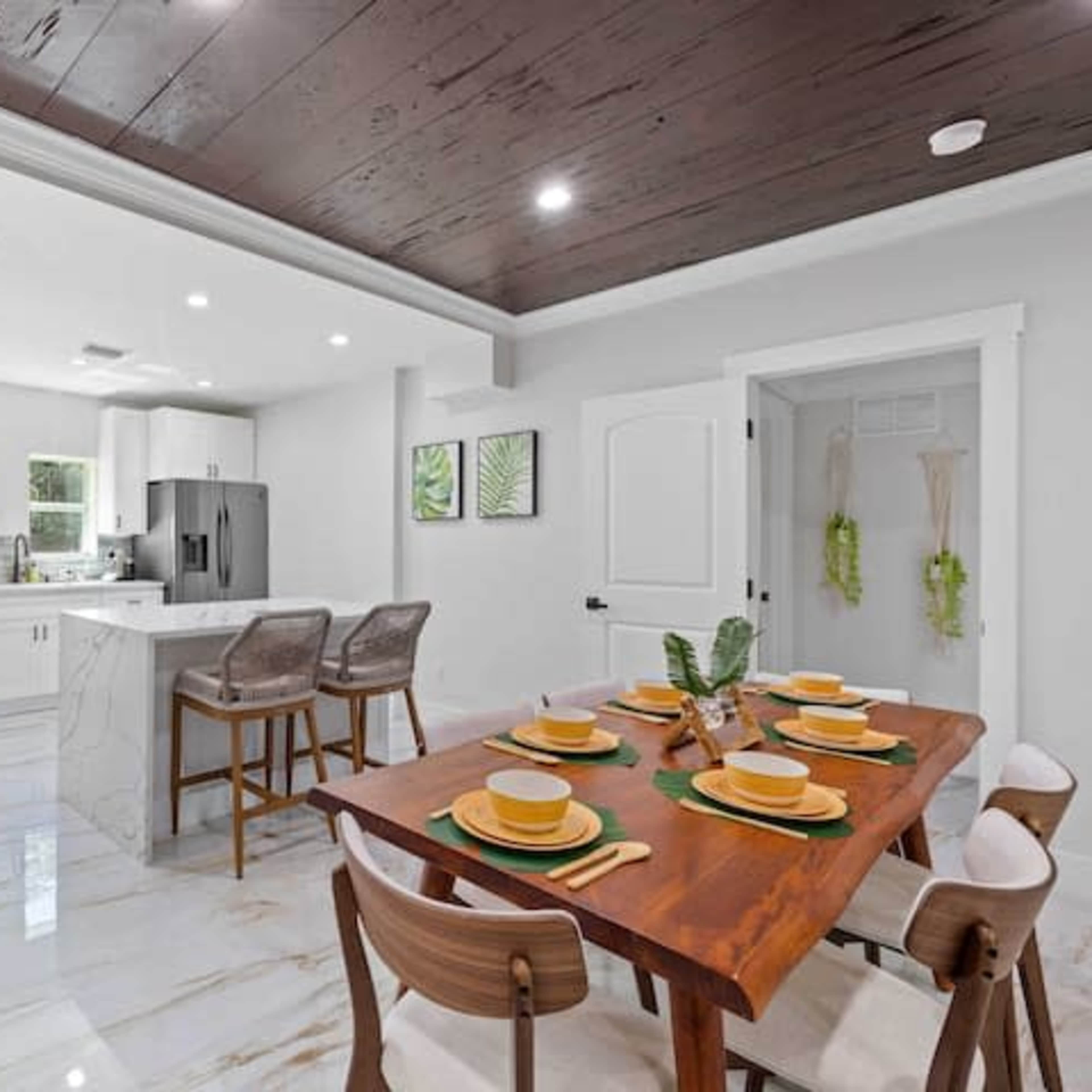 A dining area with a wooden table set for six, adjacent to a modern kitchen featuring stainless steel appliances and a marble countertop.