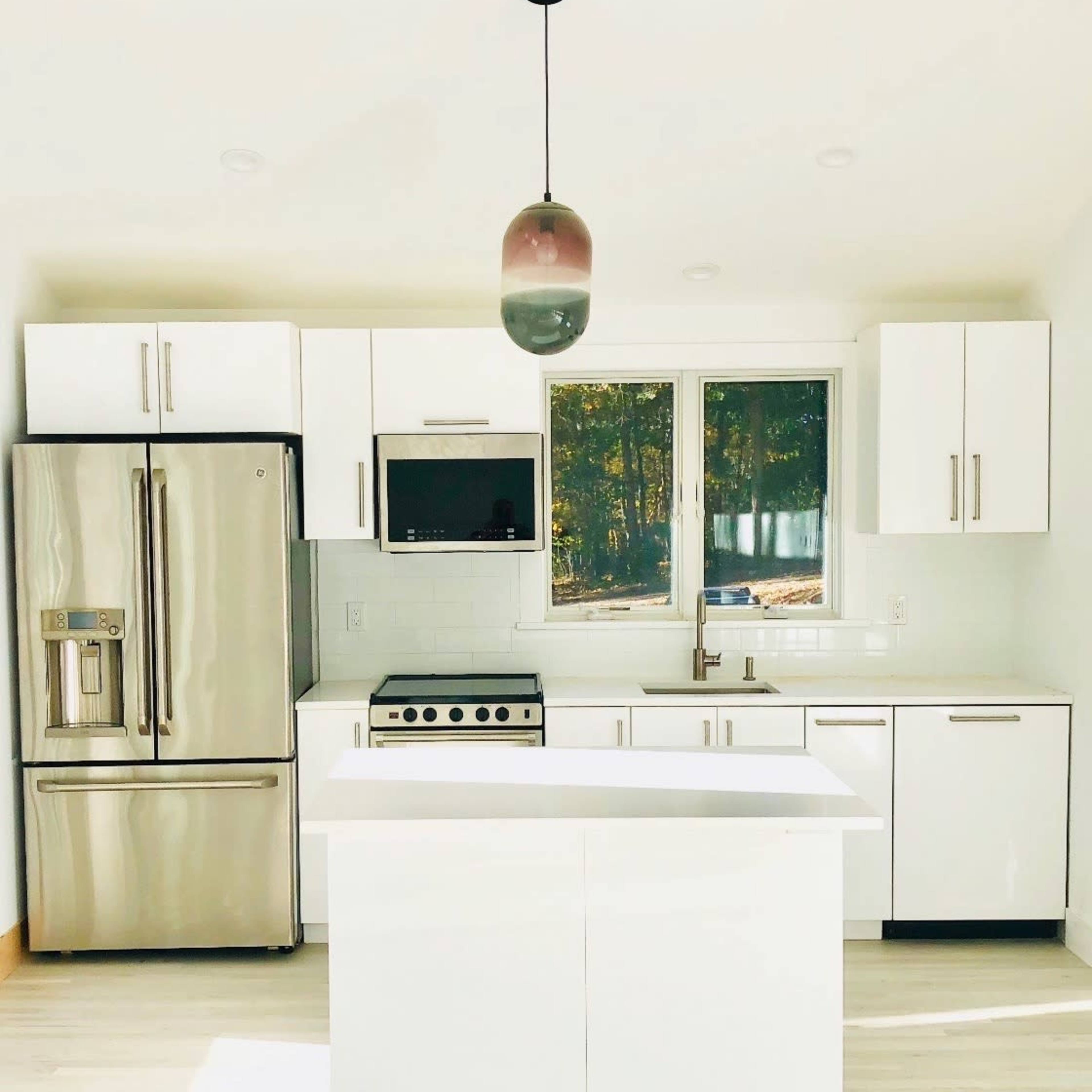 A modern kitchen with white cabinets, stainless steel appliances, and a central island beneath a pendant light.