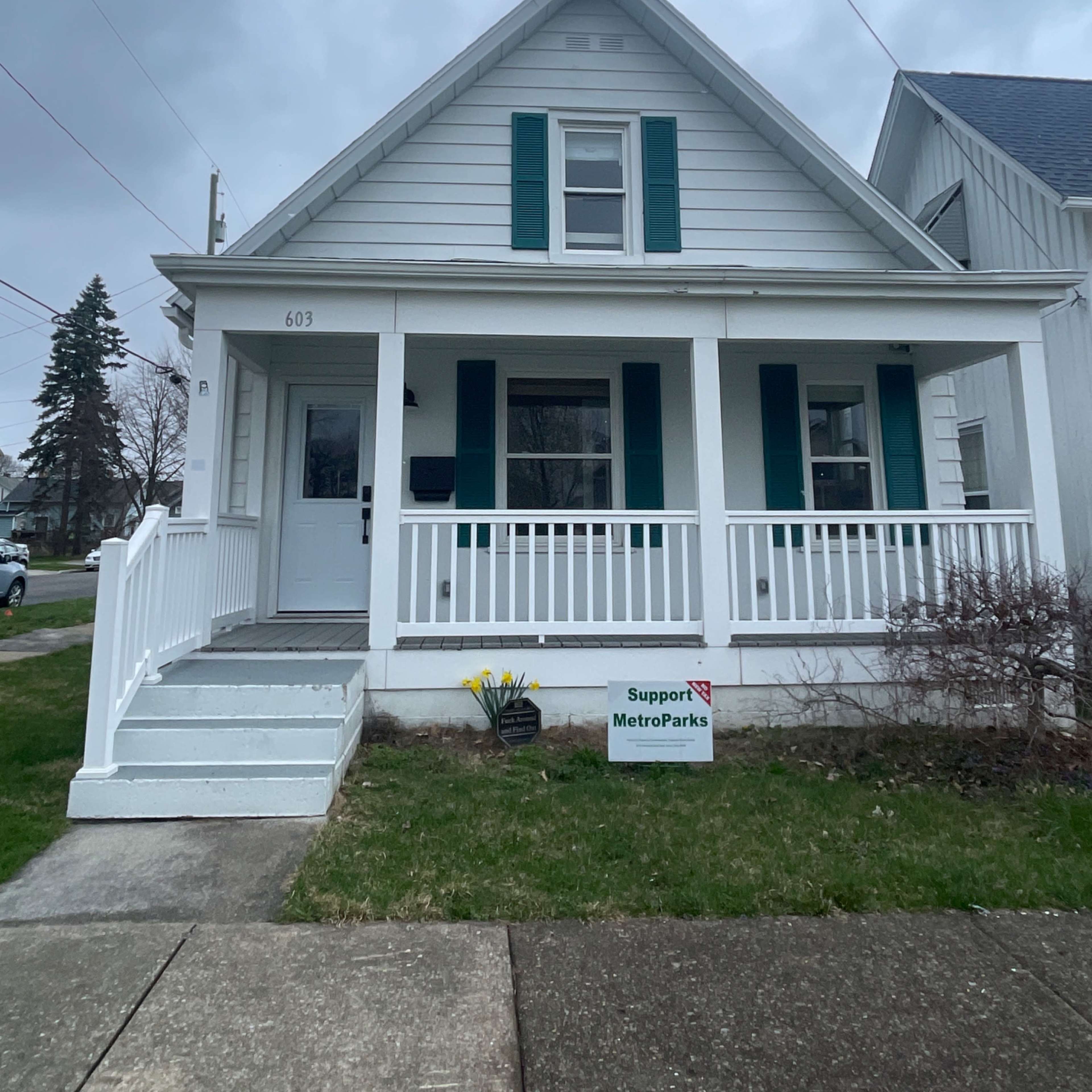 A two-story, white house with teal shutters and a front porch, located at 603, along with a sign supporting MetroParks in the yard.