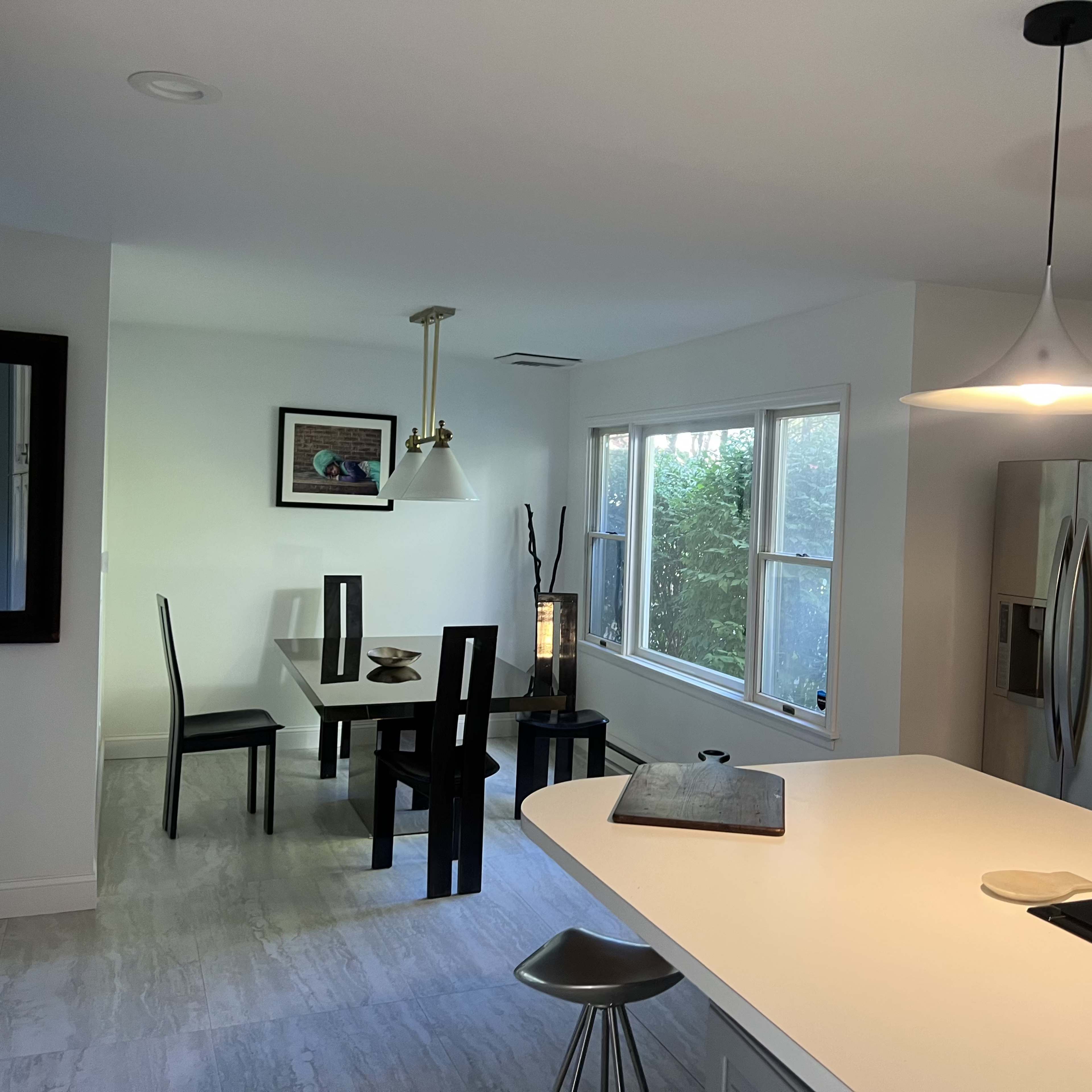 A modern kitchen and dining area featuring a white countertop, a dining table with black chairs, and large windows allowing natural light.
