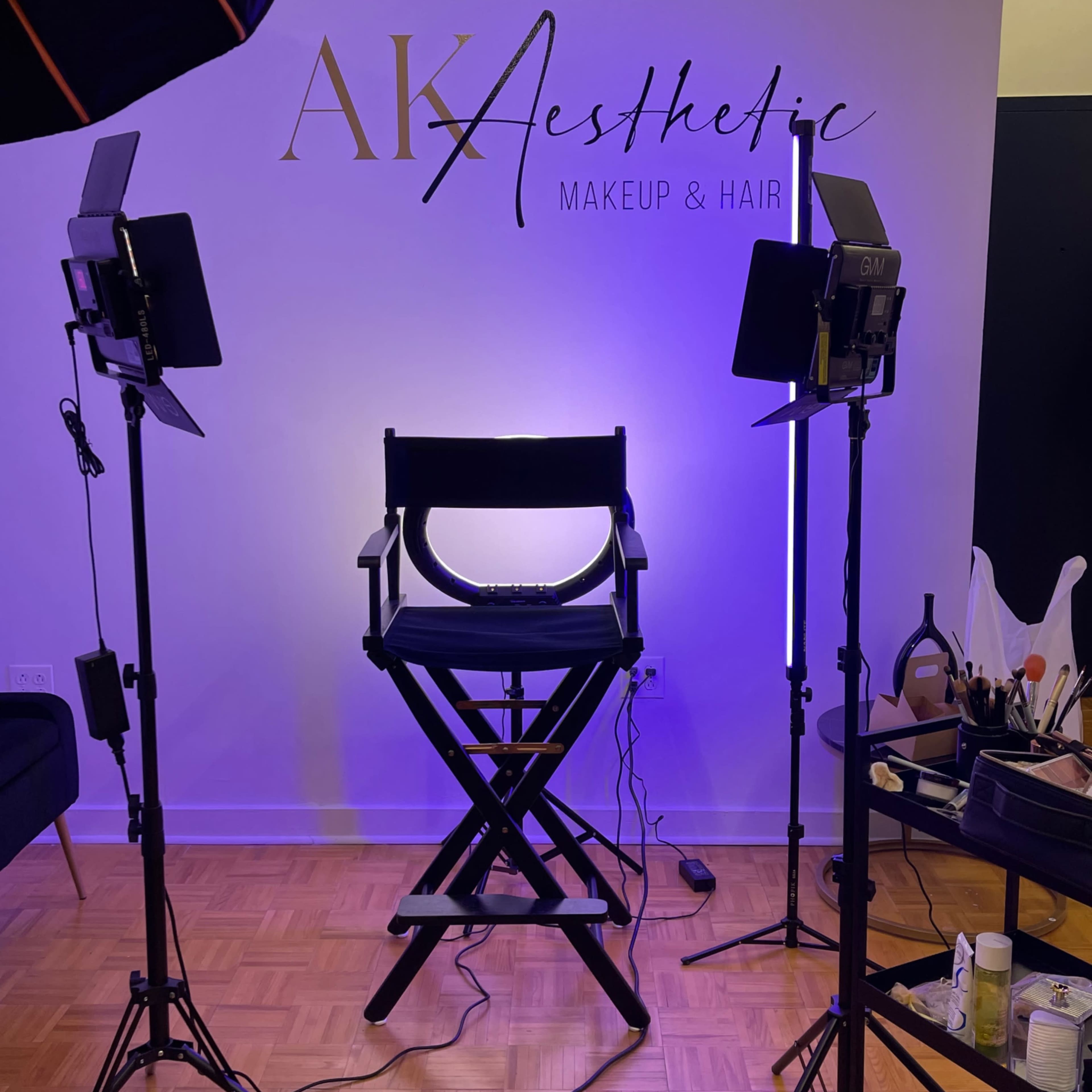 A makeup and hair studio with a director's chair positioned under soft lighting and surrounded by professional lighting equipment.