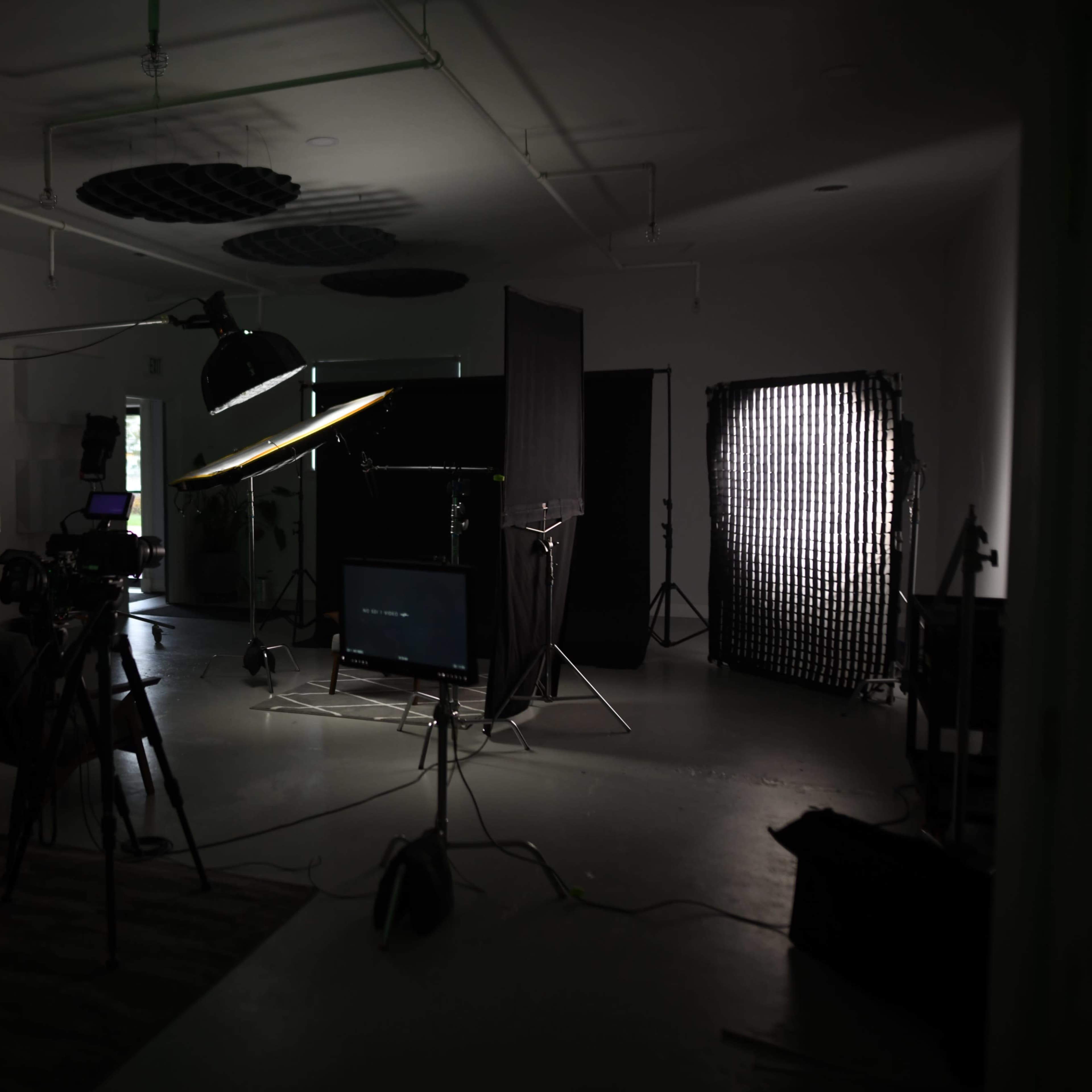 A dimly lit studio equipped with various lighting setups, cameras, and a backdrop for video production.