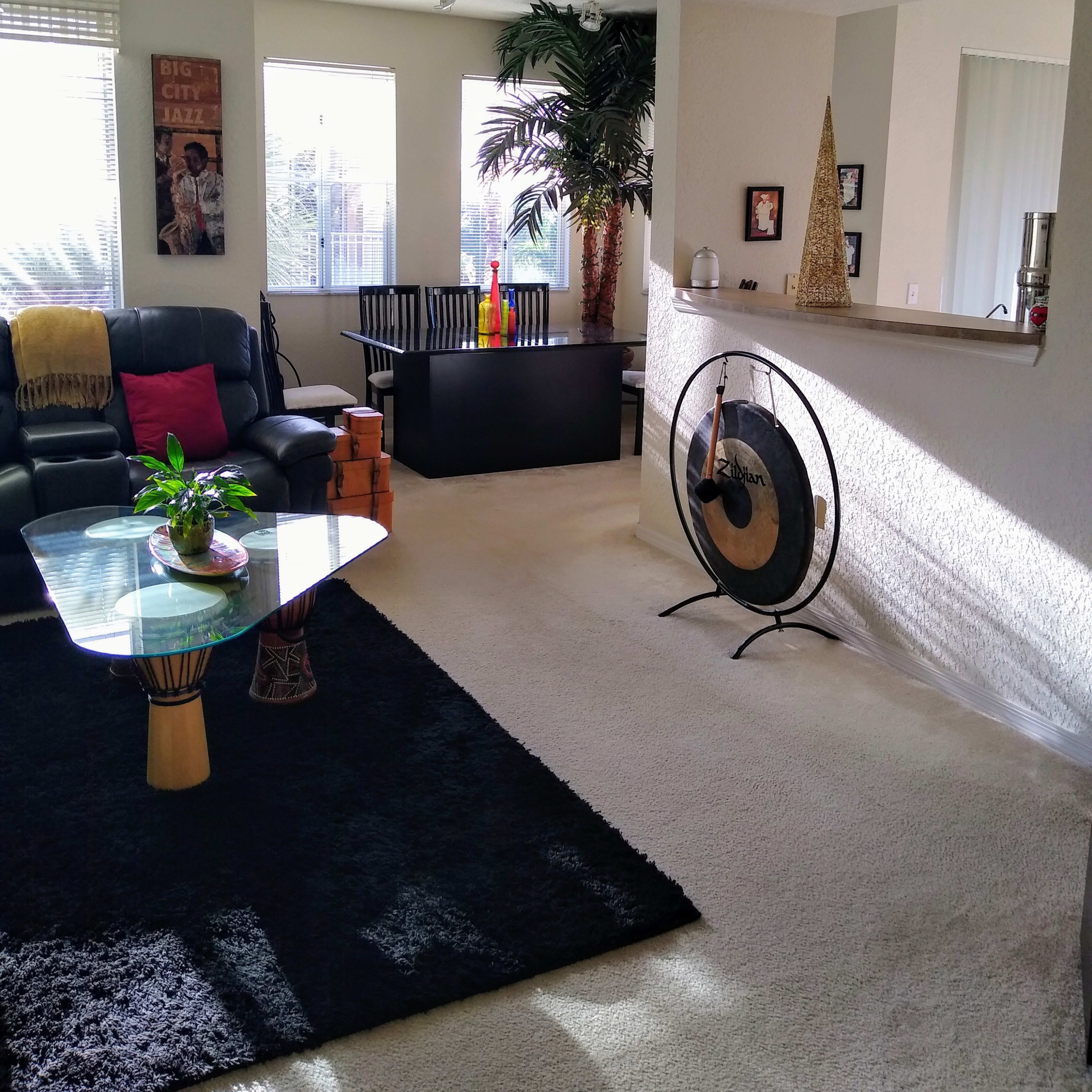 A bright living area featuring a black rug, a glass coffee table, a leather couch, and a kitchenette with decorative items.