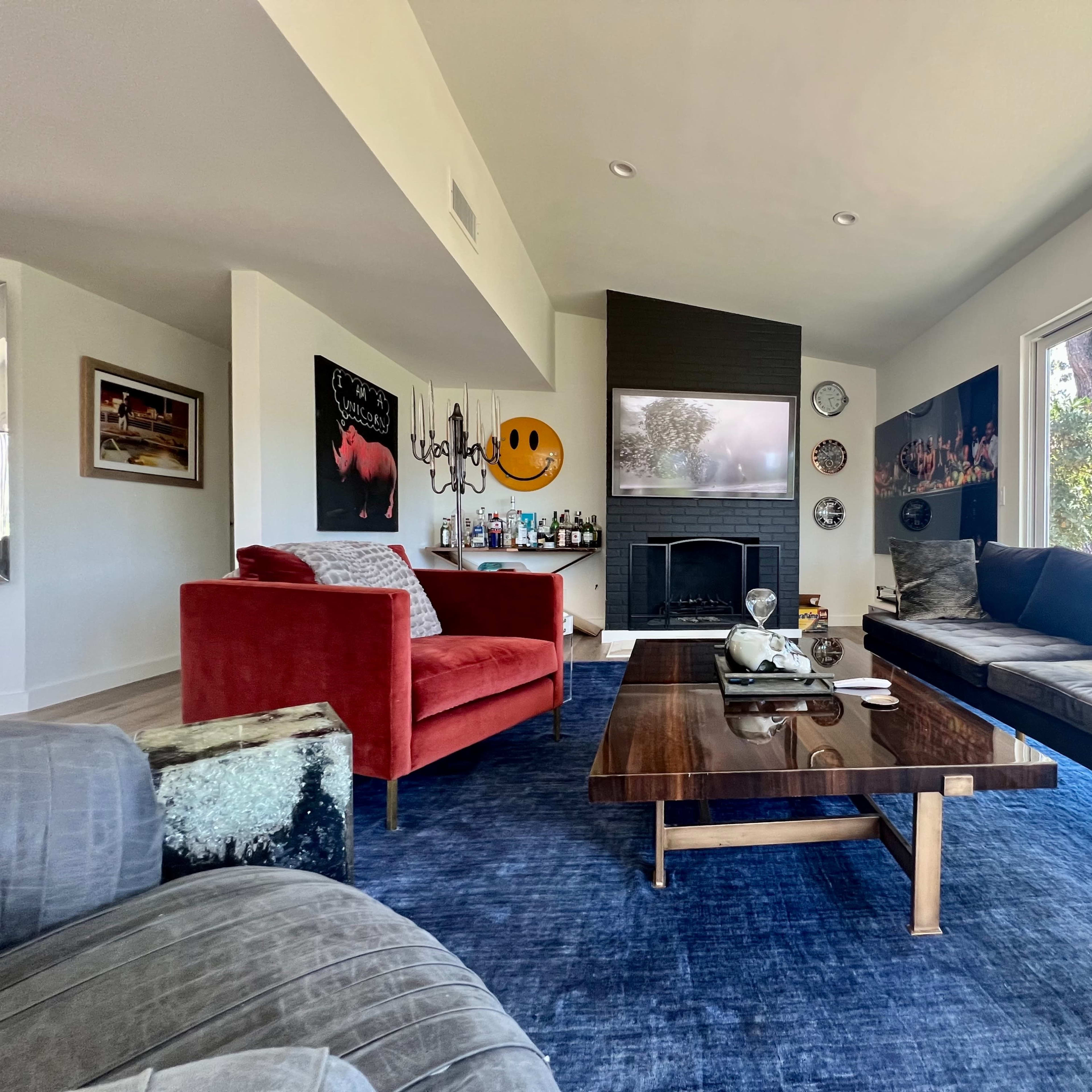 The living room features a red and dark gray sofa arrangement, a wooden coffee table, and large windows revealing outdoor views.