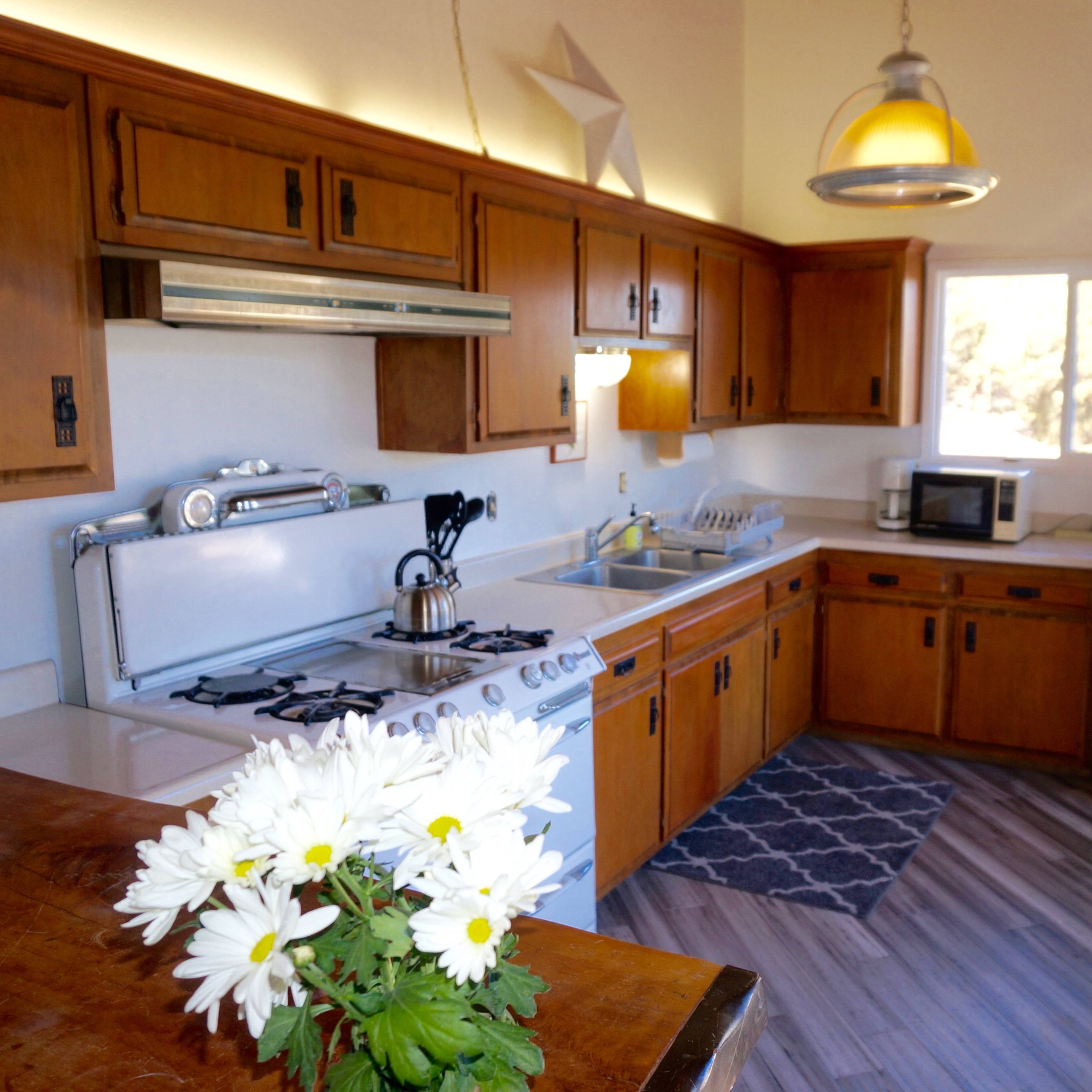 A kitchen featuring wooden cabinets, a white gas stove, a microwave, and a refrigerator under a pendant light.