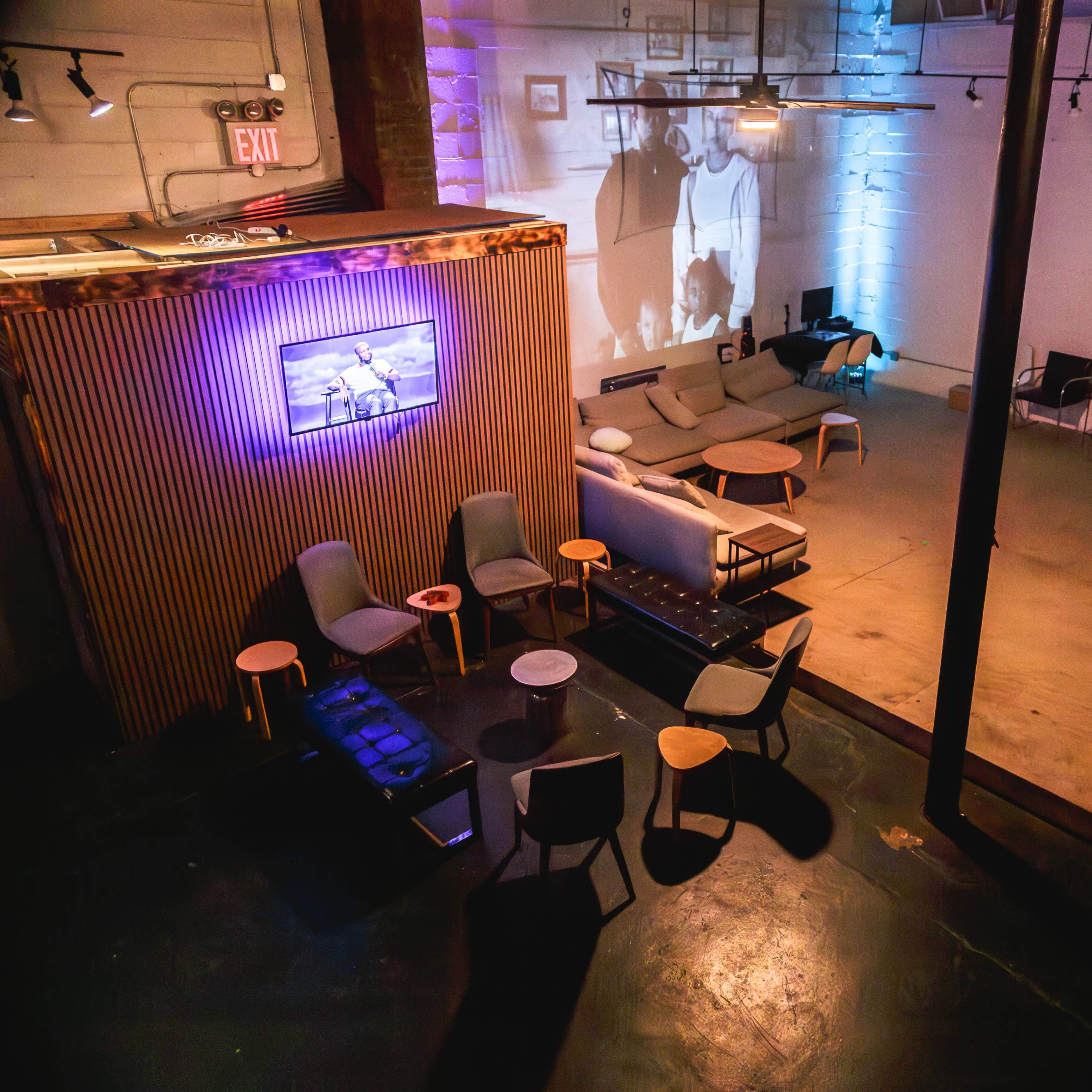 A spacious indoor lounge with seating areas, tables, and a large projection on the wall.