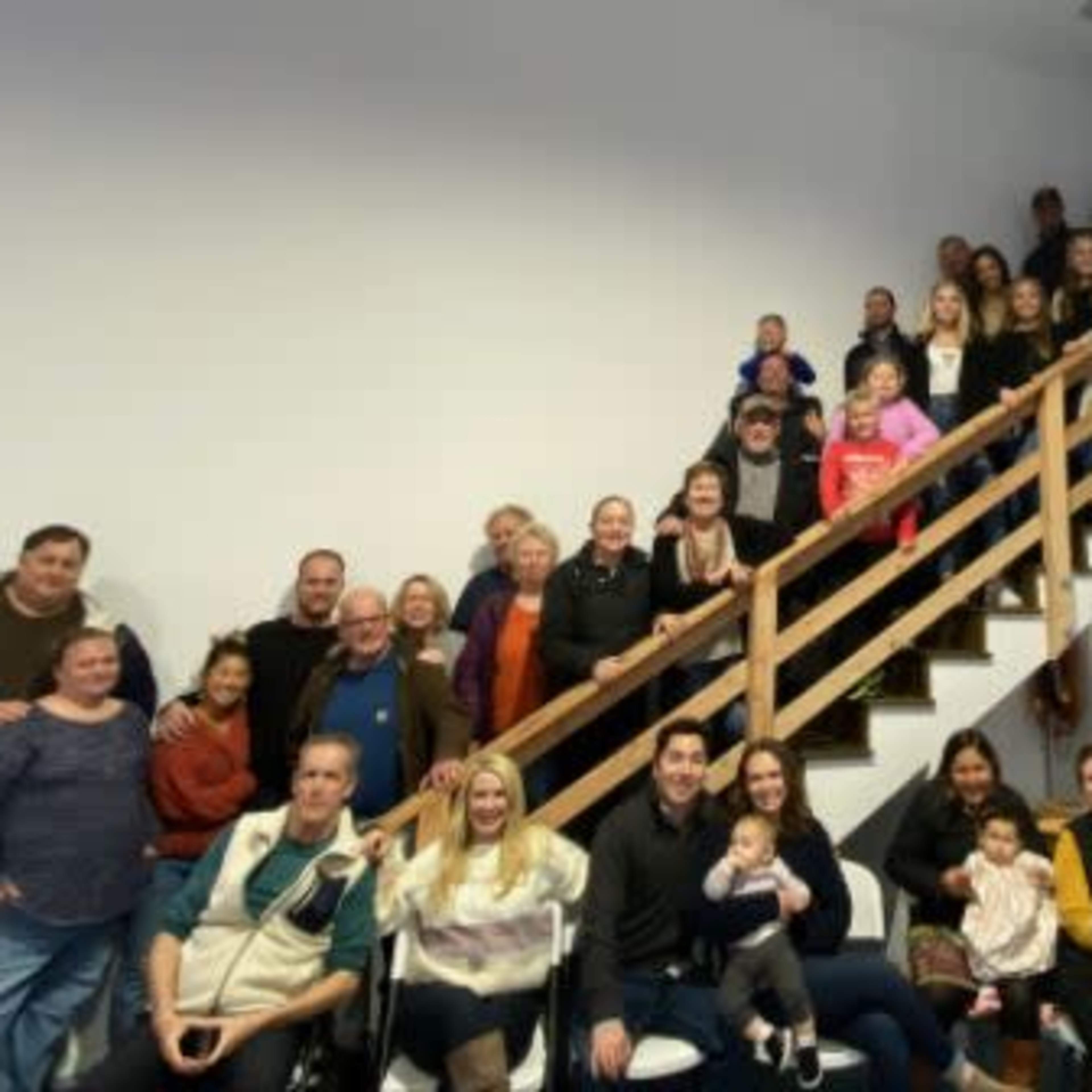 A large group of people of varying ages poses together on and around a staircase in a well-lit indoor space.