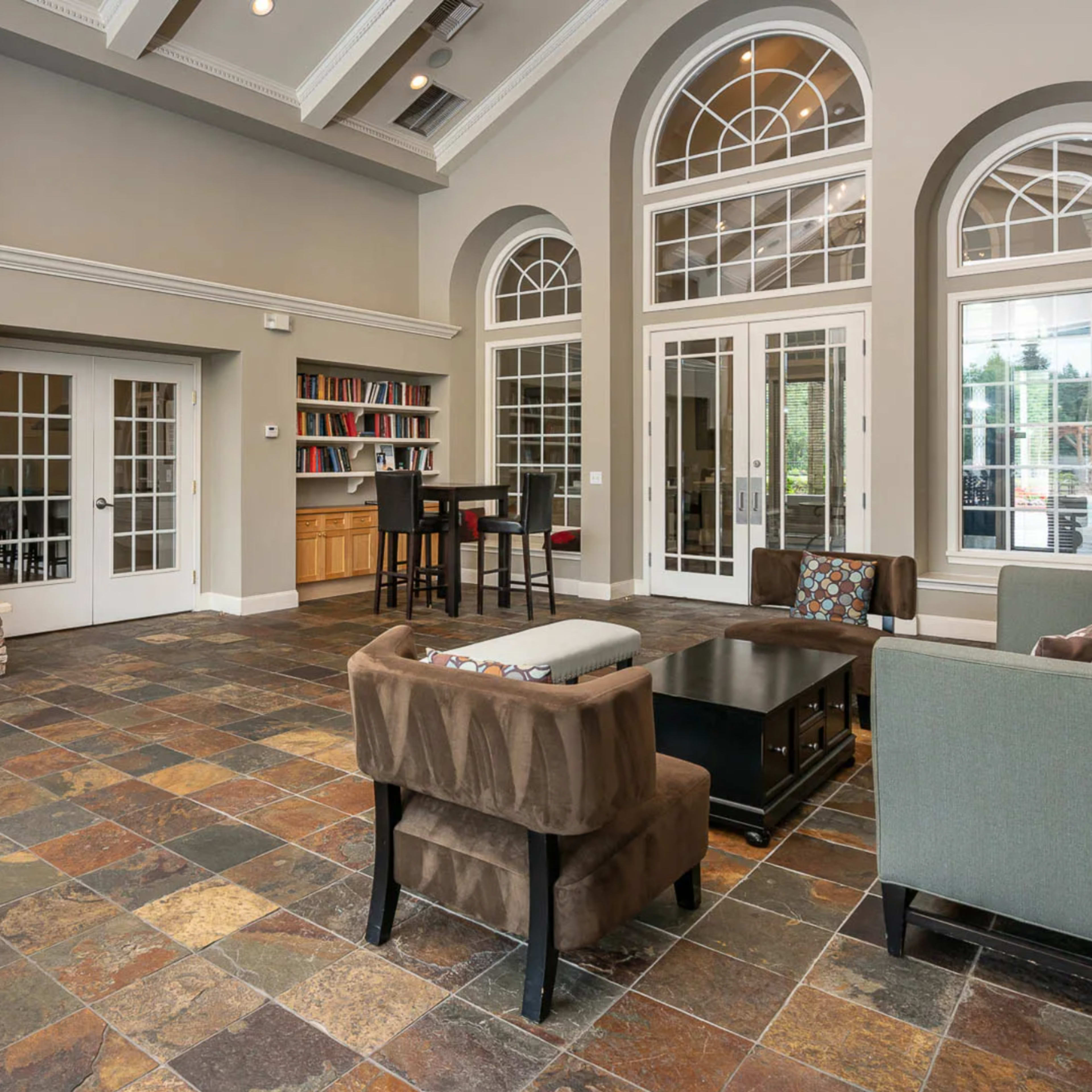 The room features a stone fireplace, large arched windows, and a seating area with a coffee table and bookshelves.