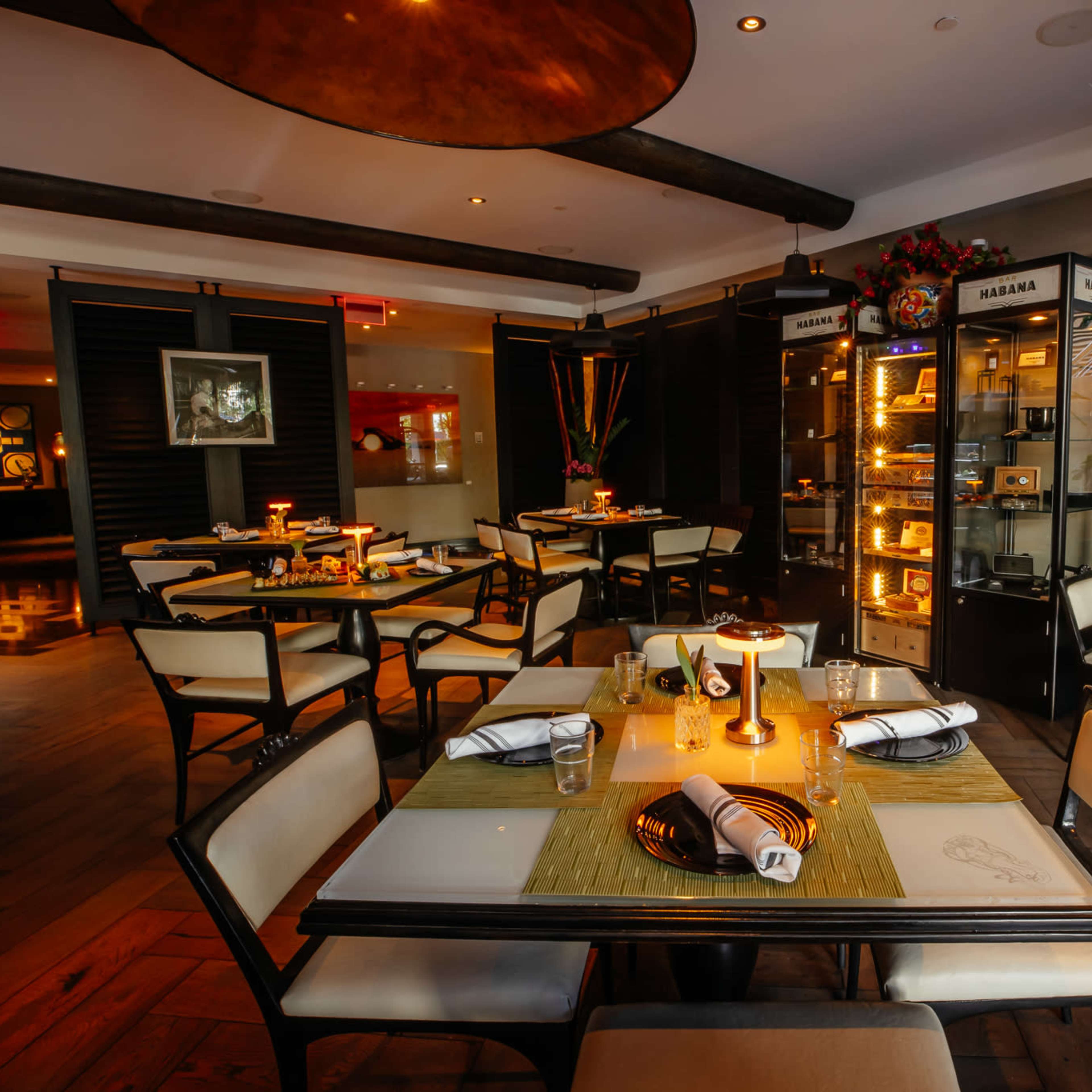 A modern restaurant interior with tables set for dining, featuring a combination of dark and light décor, and a display cabinet showcasing various items.