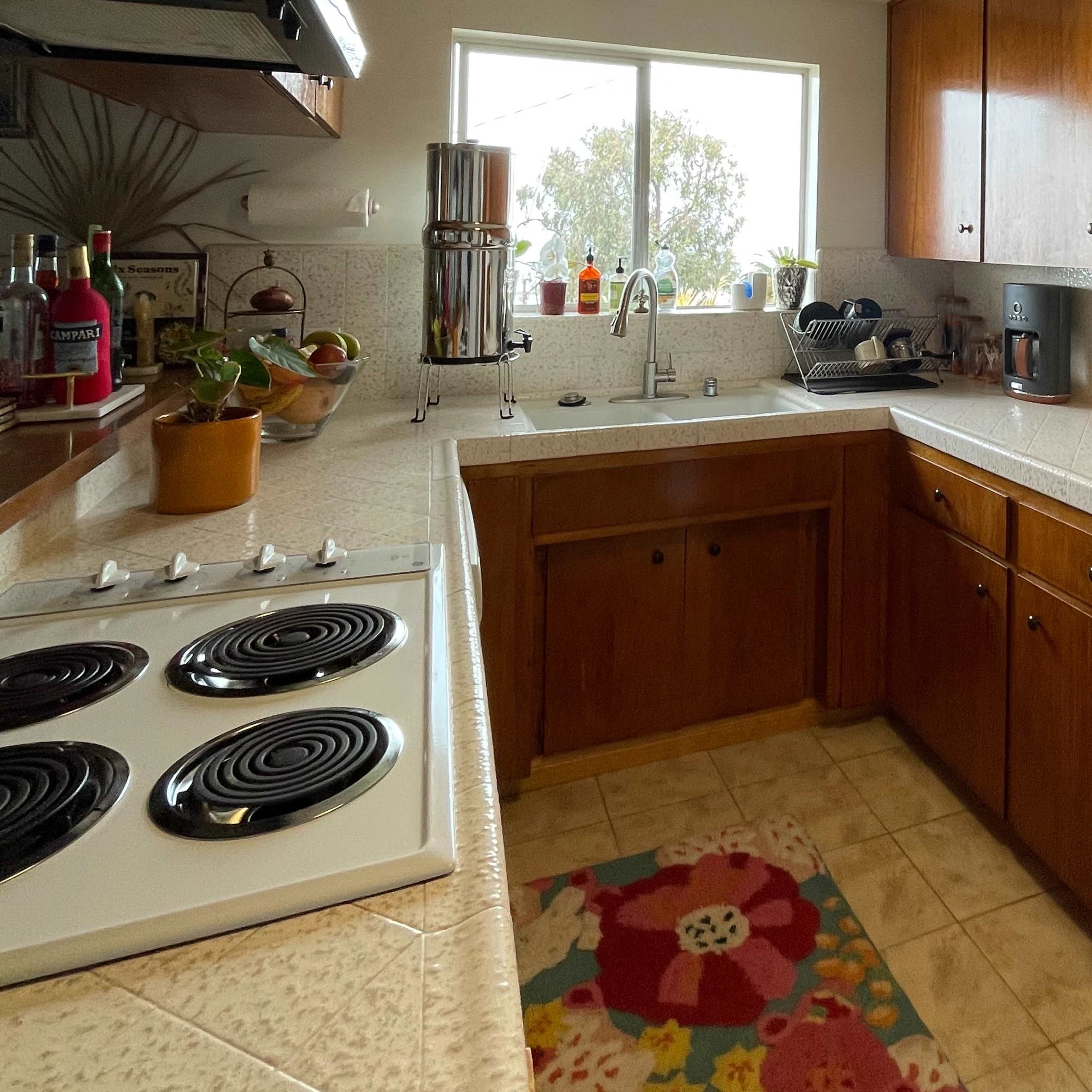 A compact kitchen with wooden cabinets, a sink under a window, and a stove with black burners.