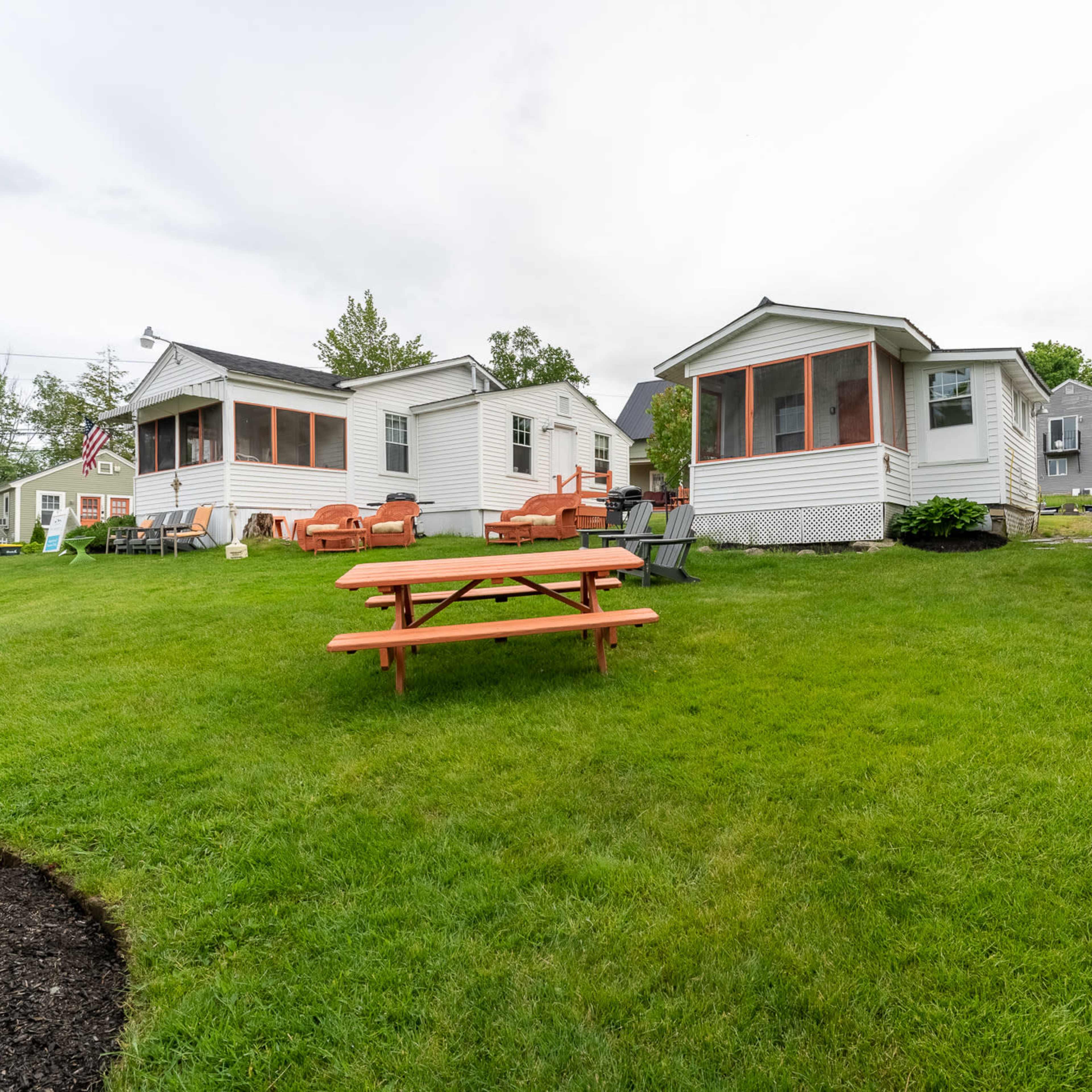 Several vacation cottages arranged on a grassy area, with picnic tables and lawn chairs scattered around.