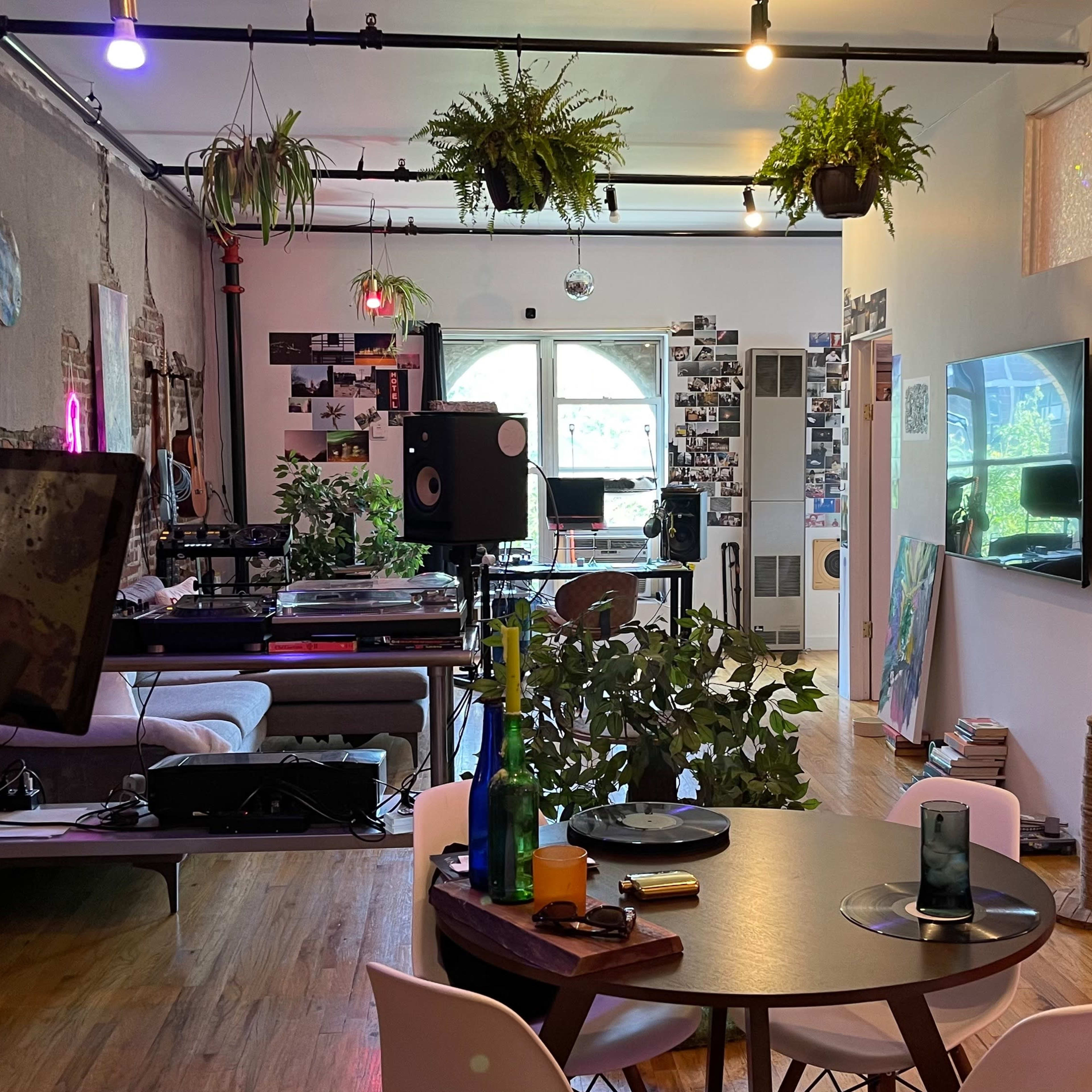 An interior space featuring a dining table with chairs, a workout bike, plants hanging from the ceiling, and a mix of modern and artistic decor.