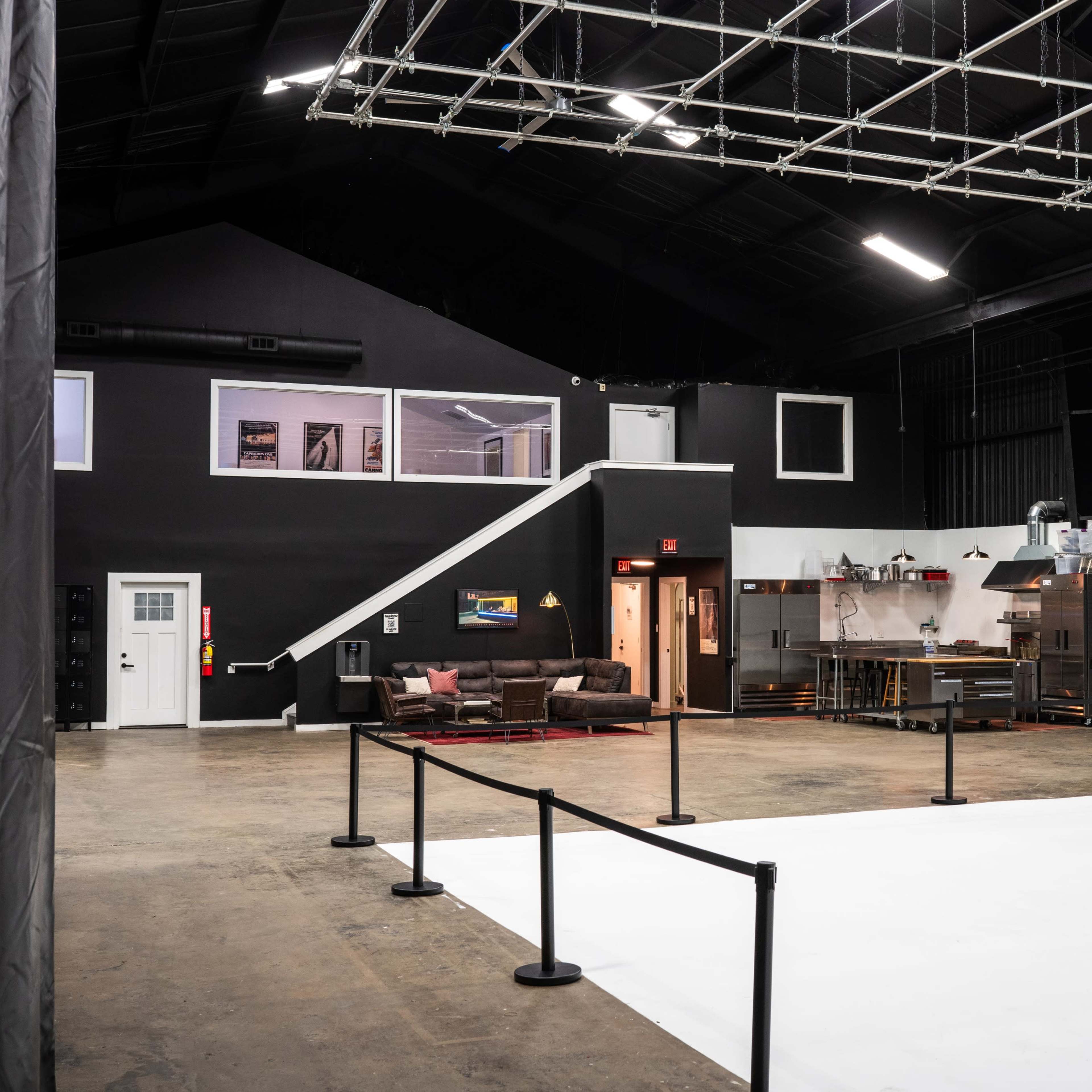 A spacious studio with a white backdrop, a lounge area on the left, and a kitchen space in the background.