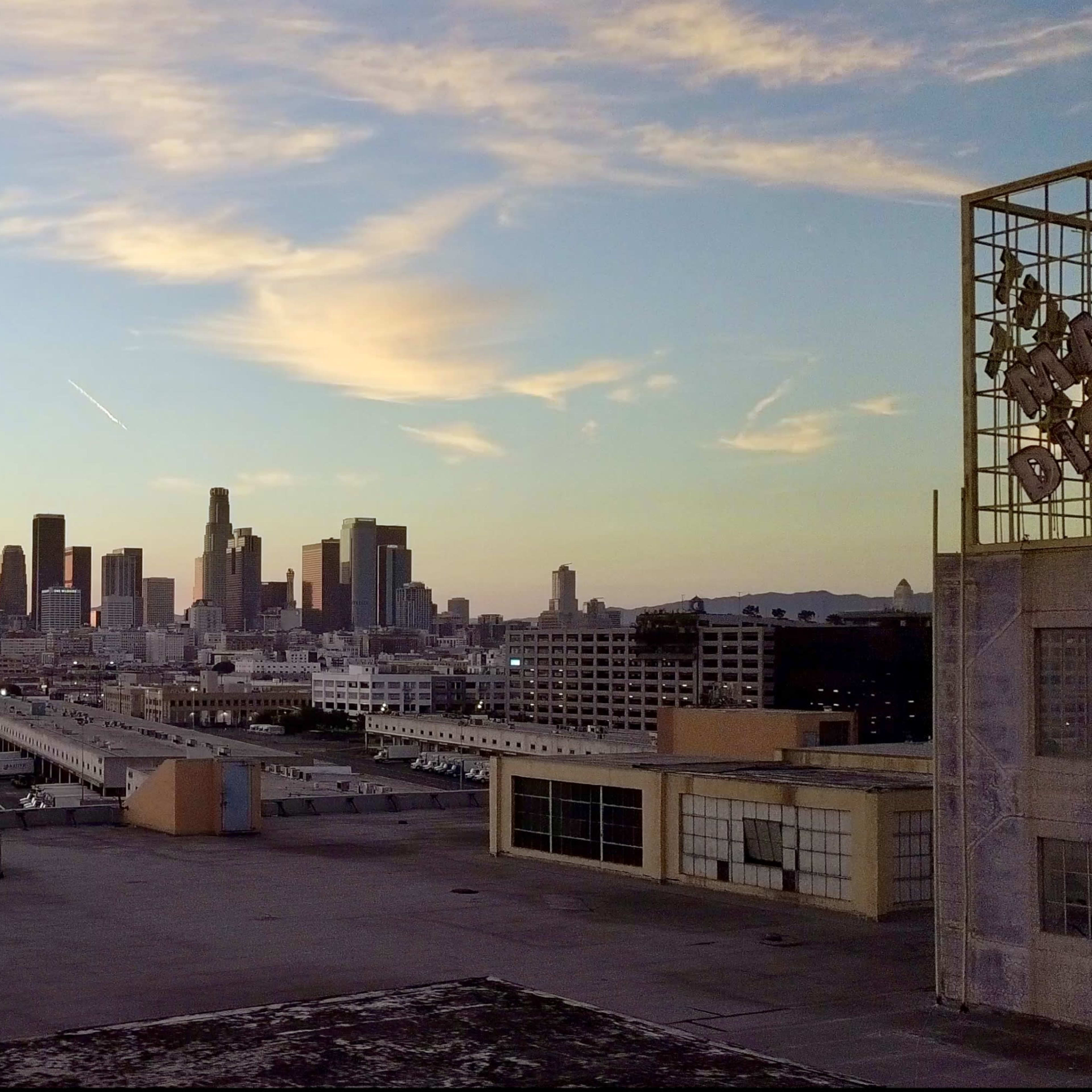 The skyline of Los Angeles at sunset, with buildings in the foreground and a colorful sky above.