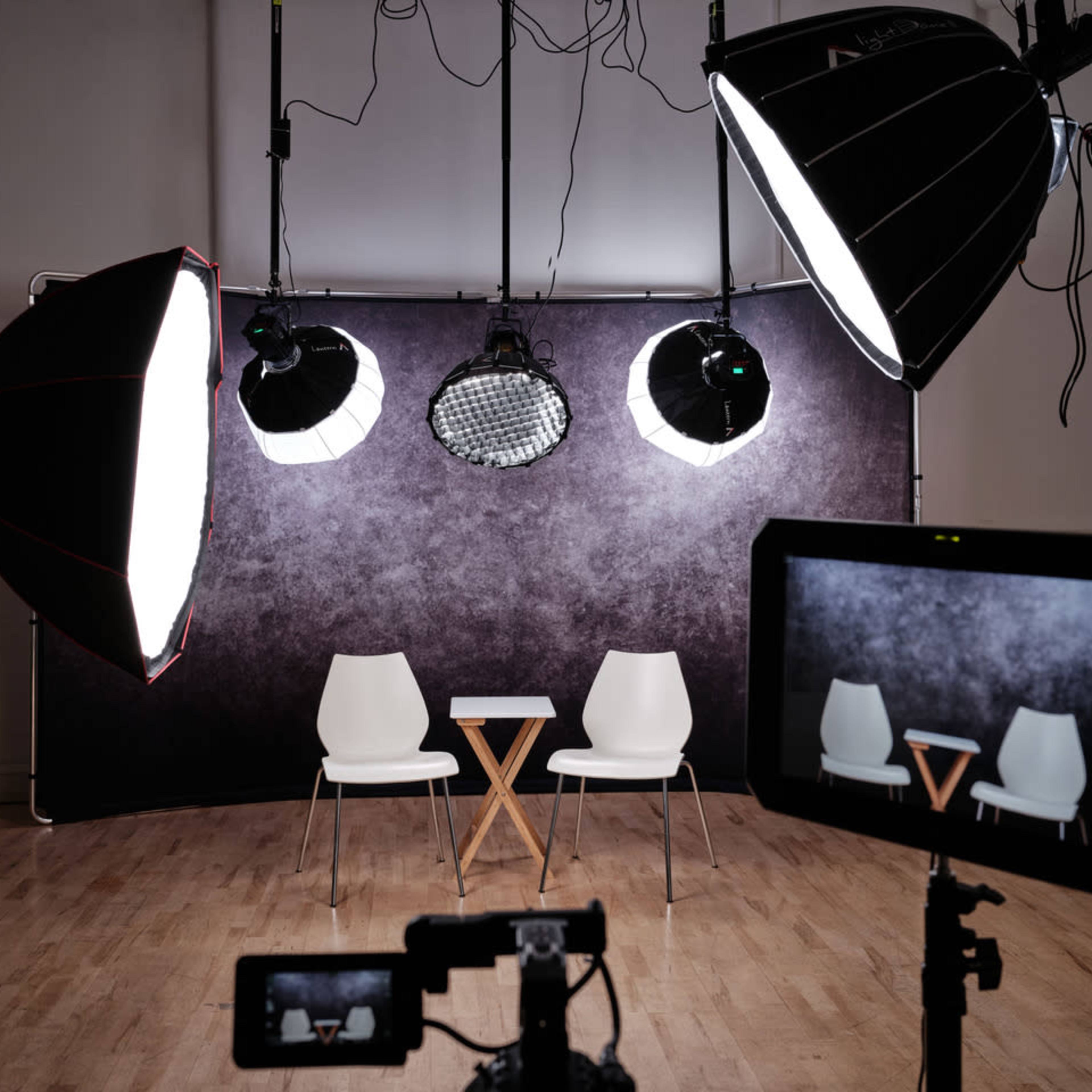 A photography setup with two white chairs and a small table illuminated by multiple studio lights against a dark backdrop.