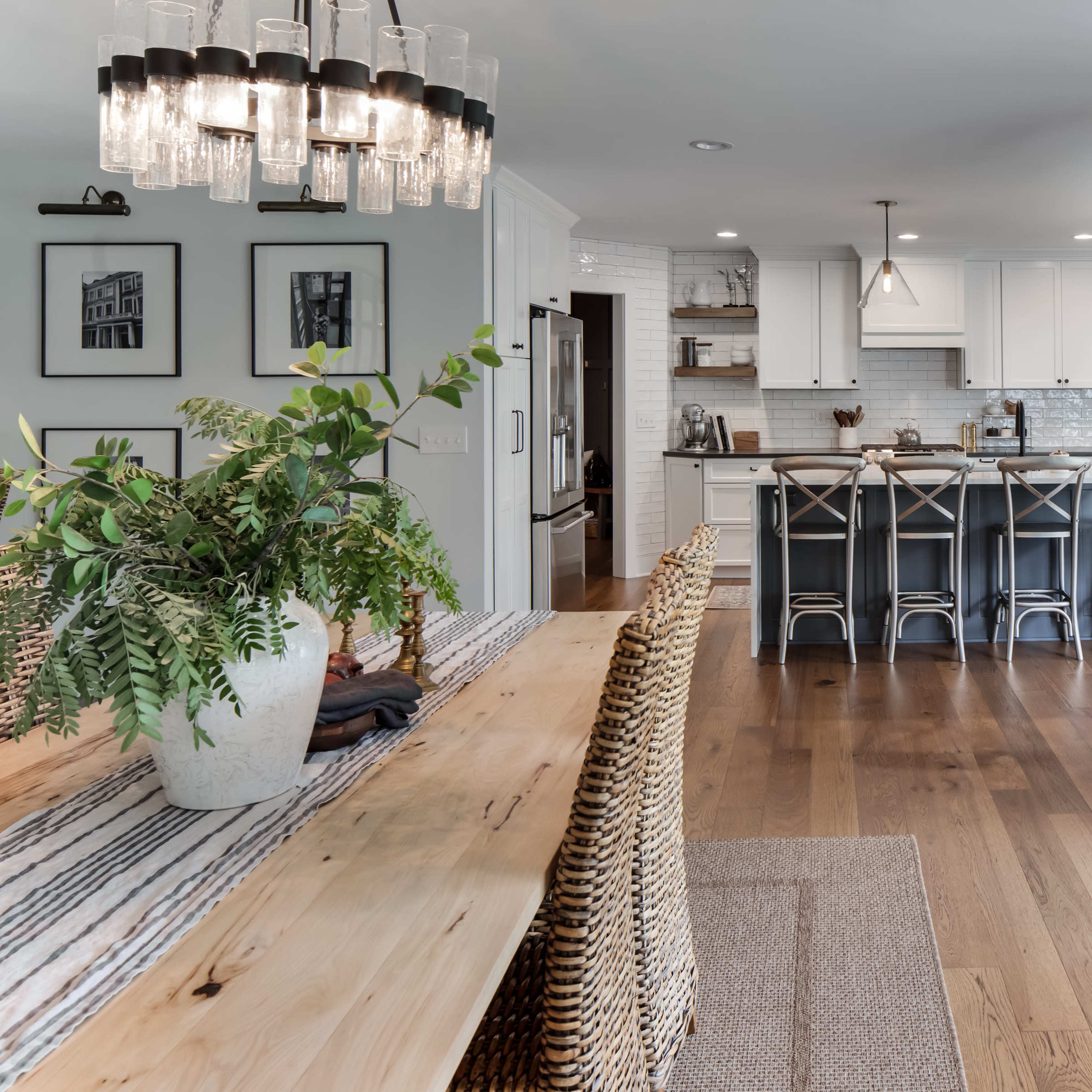 A modern kitchen and dining area with a wooden dining table, wicker chairs, and a kitchen island with bar stools.