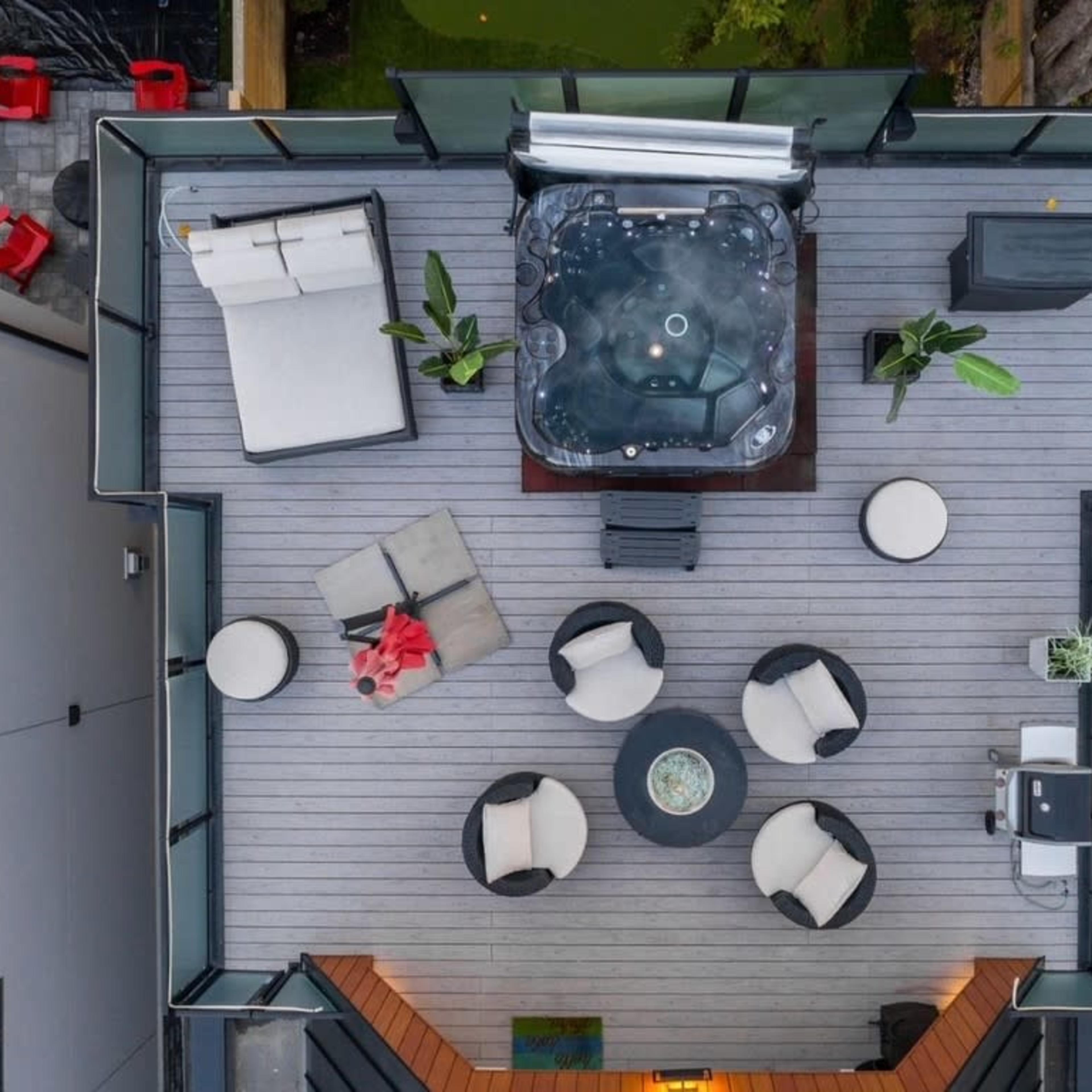 An aerial view of a rooftop deck featuring a hot tub, seating area with circular chairs, and decorative plants.