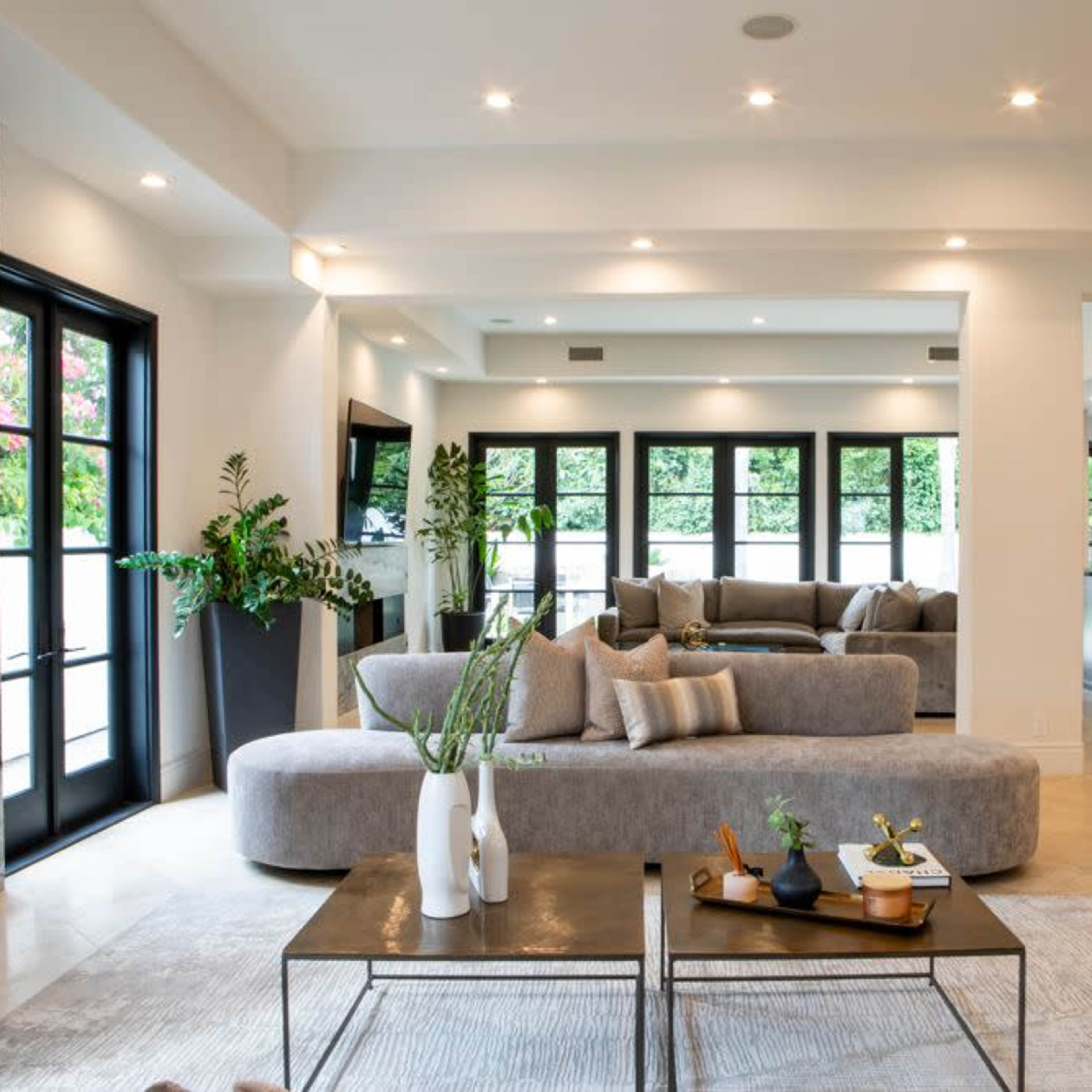 A spacious living room features sleek gray furniture, large windows, and modern decor elements.