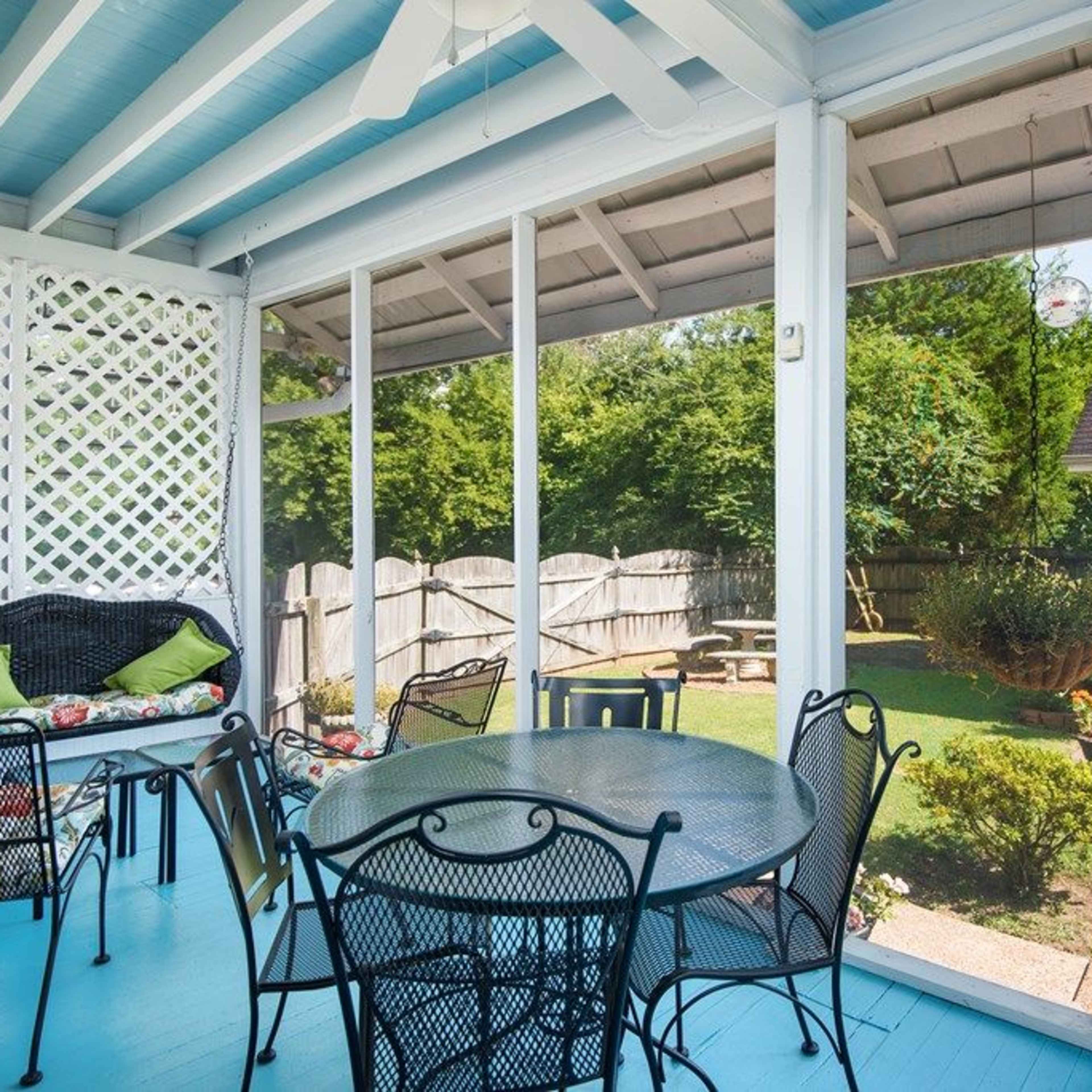 A screened porch with a black table and chairs overlooking a backyard with a wooden fence and a small shed.