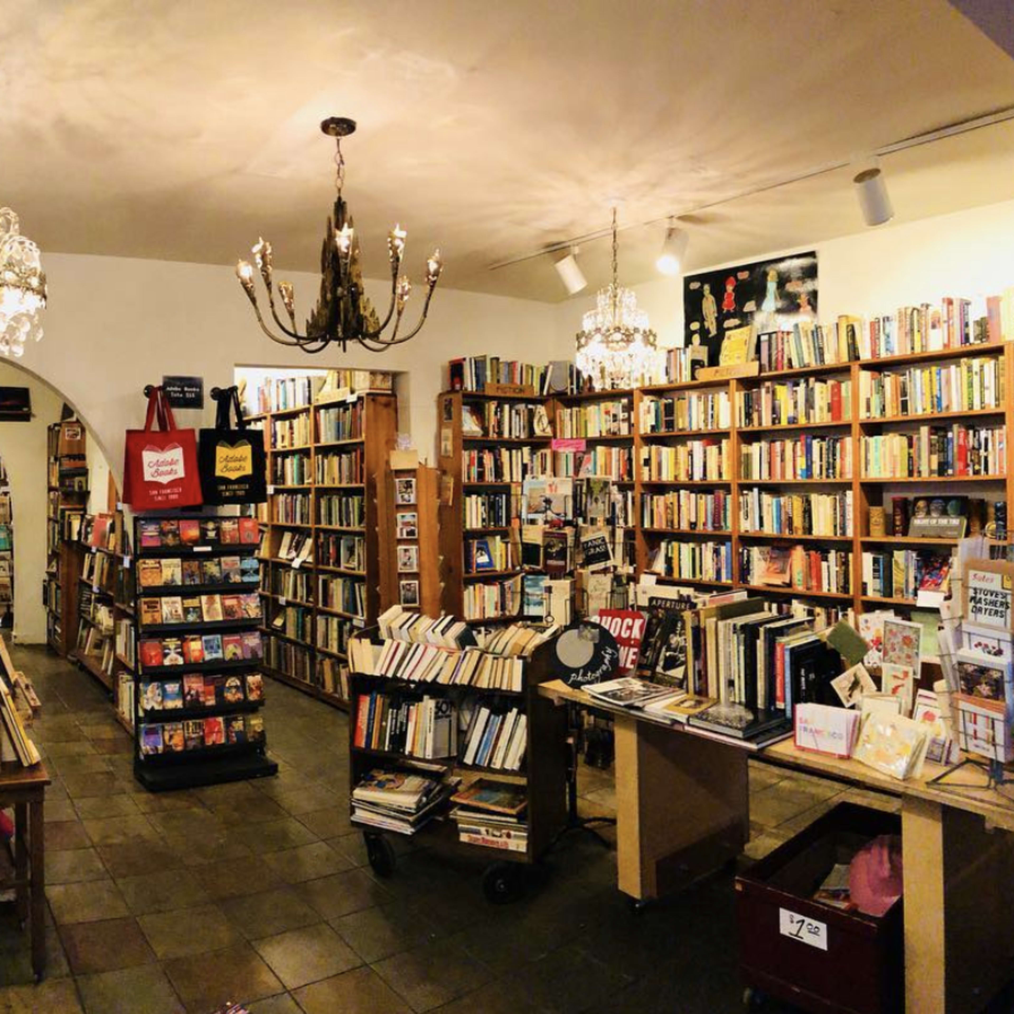 A cozy bookstore with tall bookshelves filled with books, chandeliers hanging from the ceiling, and wooden furniture scattered throughout the space.