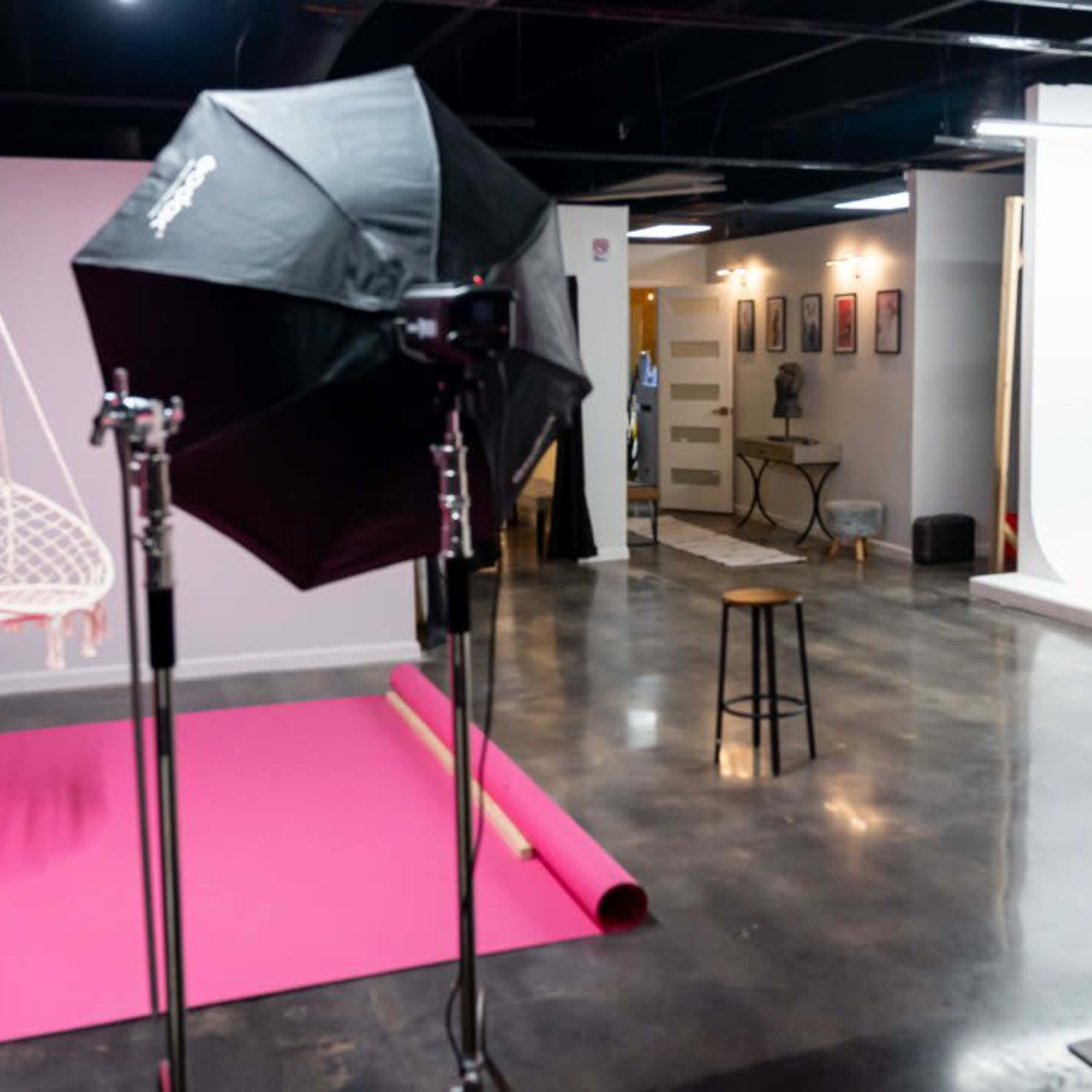 A spacious photography studio featuring a pink backdrop, a blue velvet throne, and various lighting equipment.