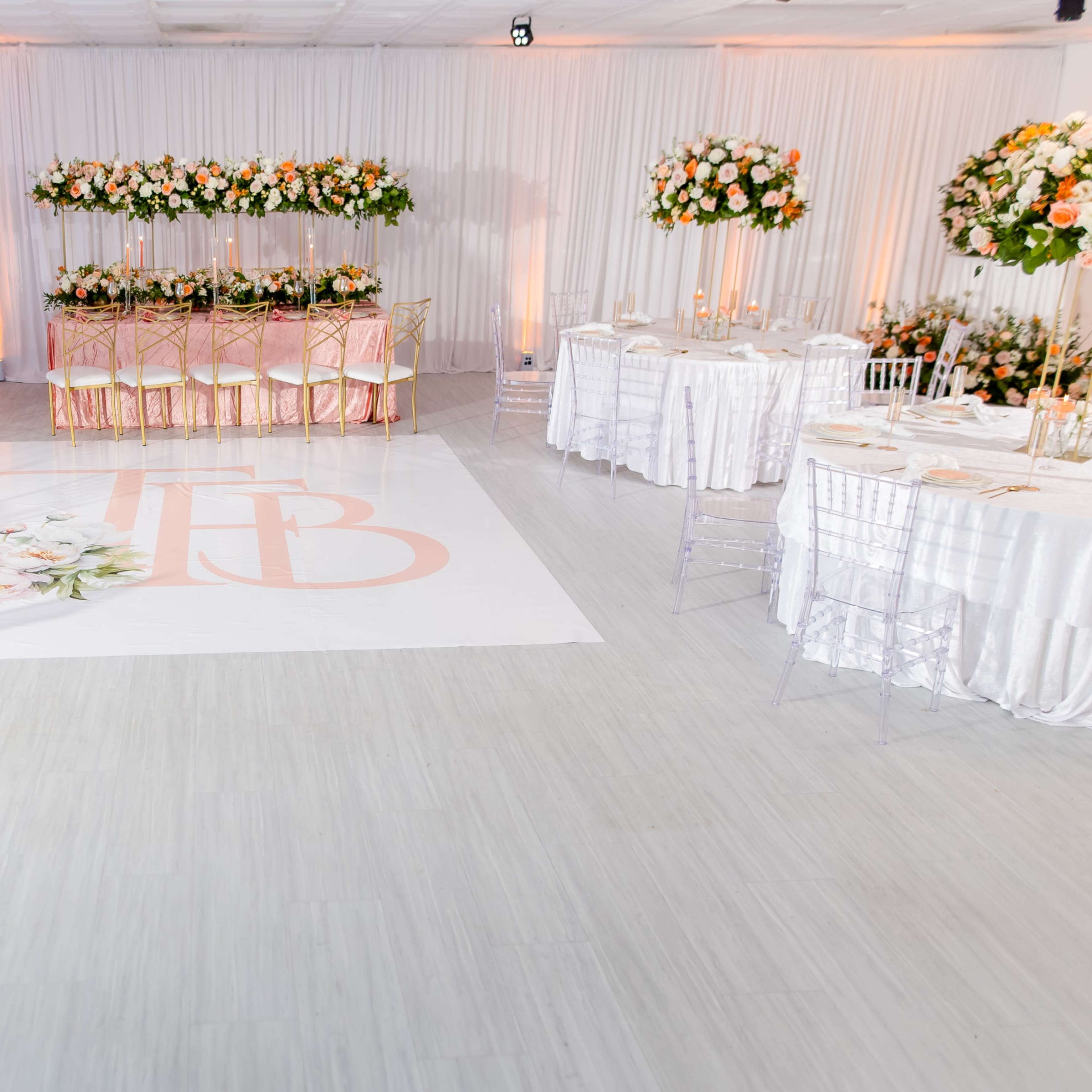 A decorated event space with floral centerpieces on tables and a large floral design on the floor featuring the letters "TB."