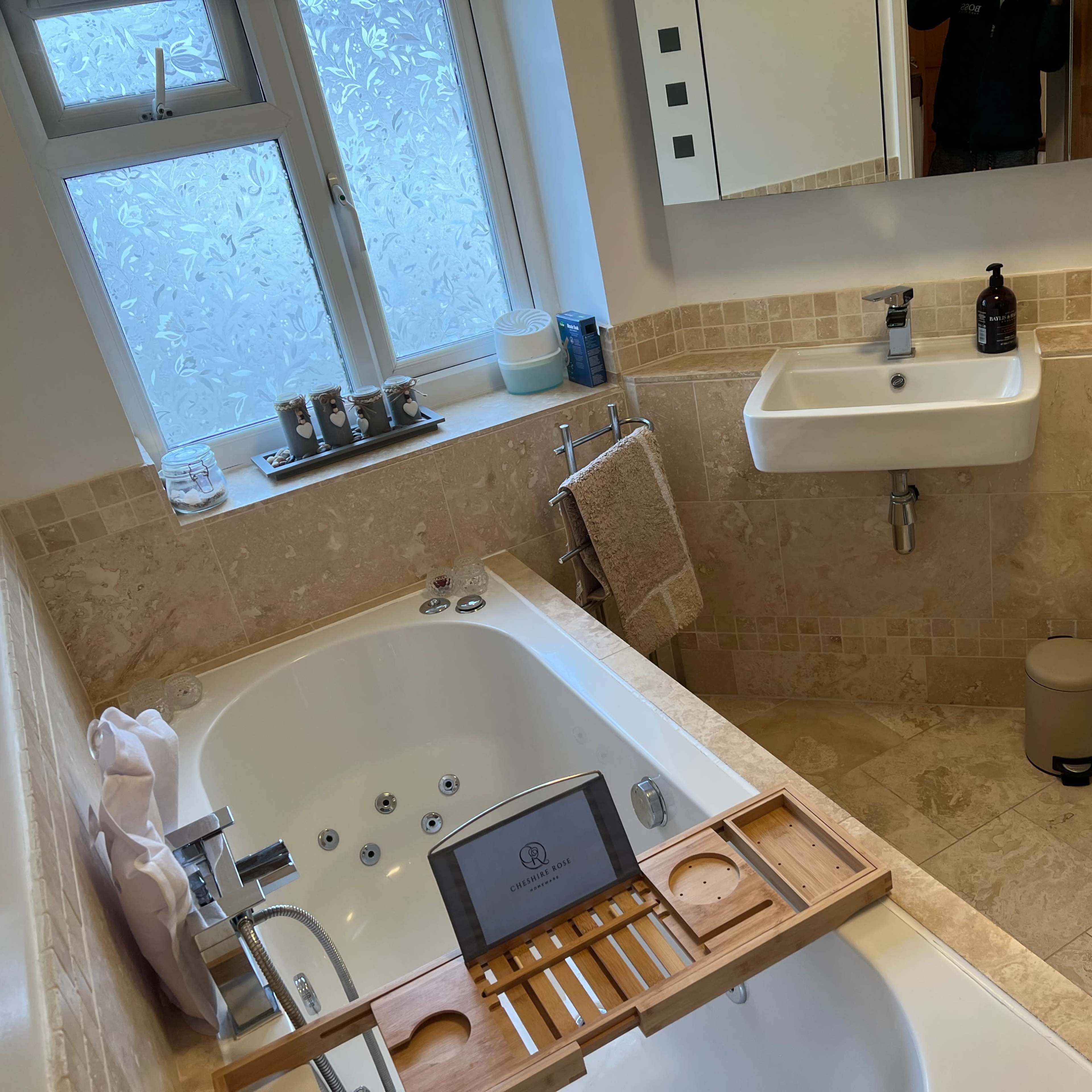 A bathroom featuring a bathtub, a wall-mounted sink, a toilet, and a window with frosted glass.