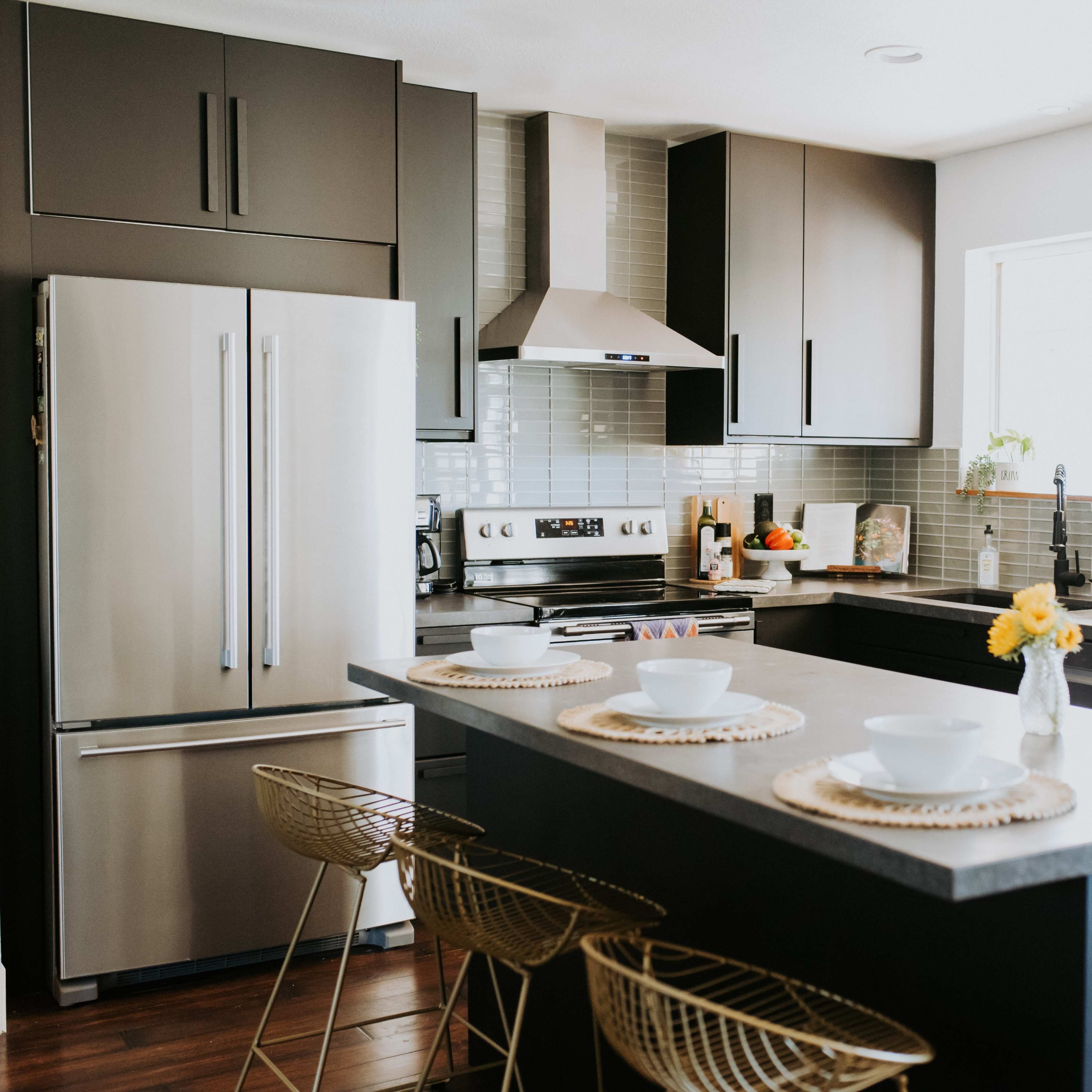 A modern kitchen features stainless steel appliances, a central island with stools, and open shelving displaying various kitchen items.