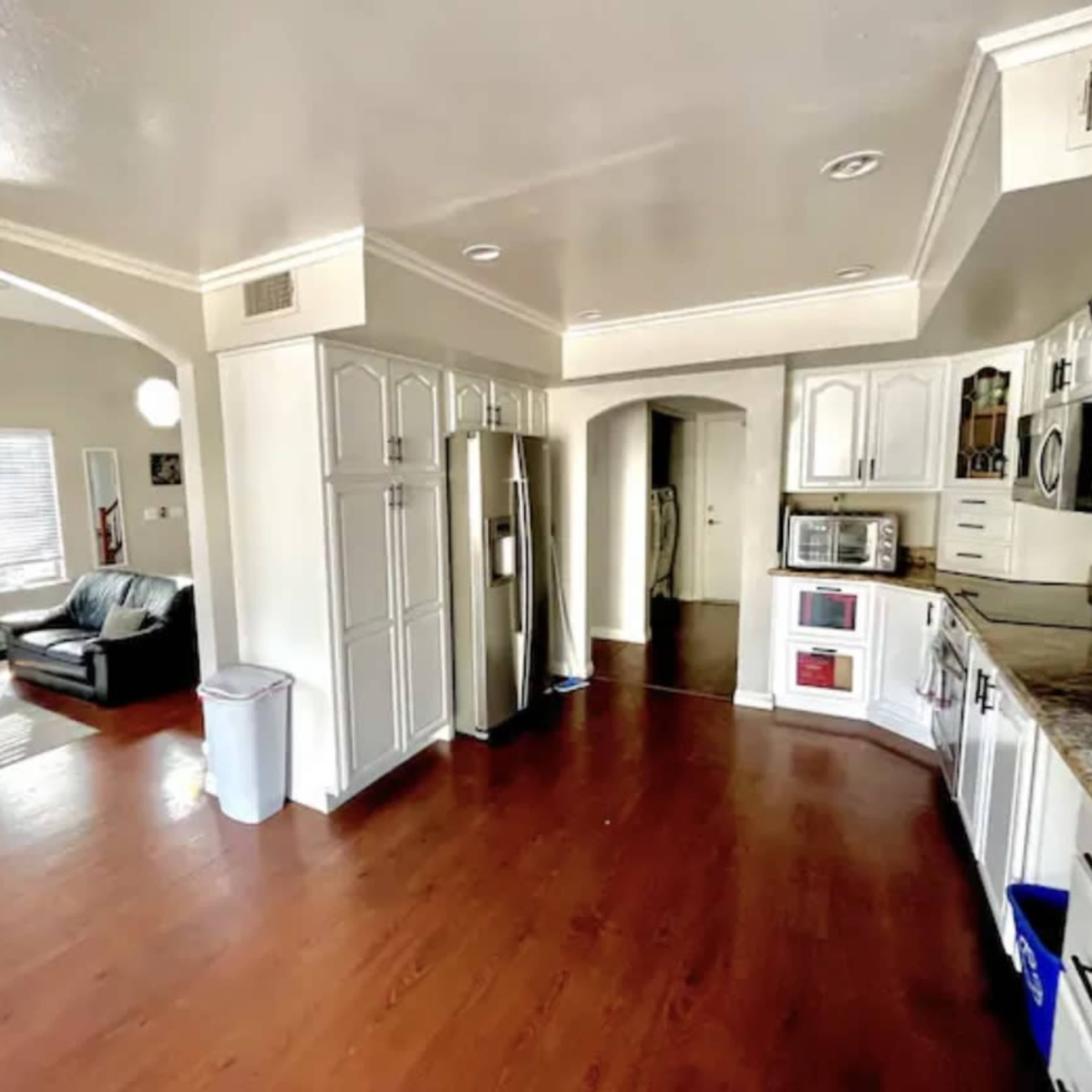 A spacious kitchen with white cabinetry and stainless steel appliances, opening into a living area featuring a fireplace and a couch.