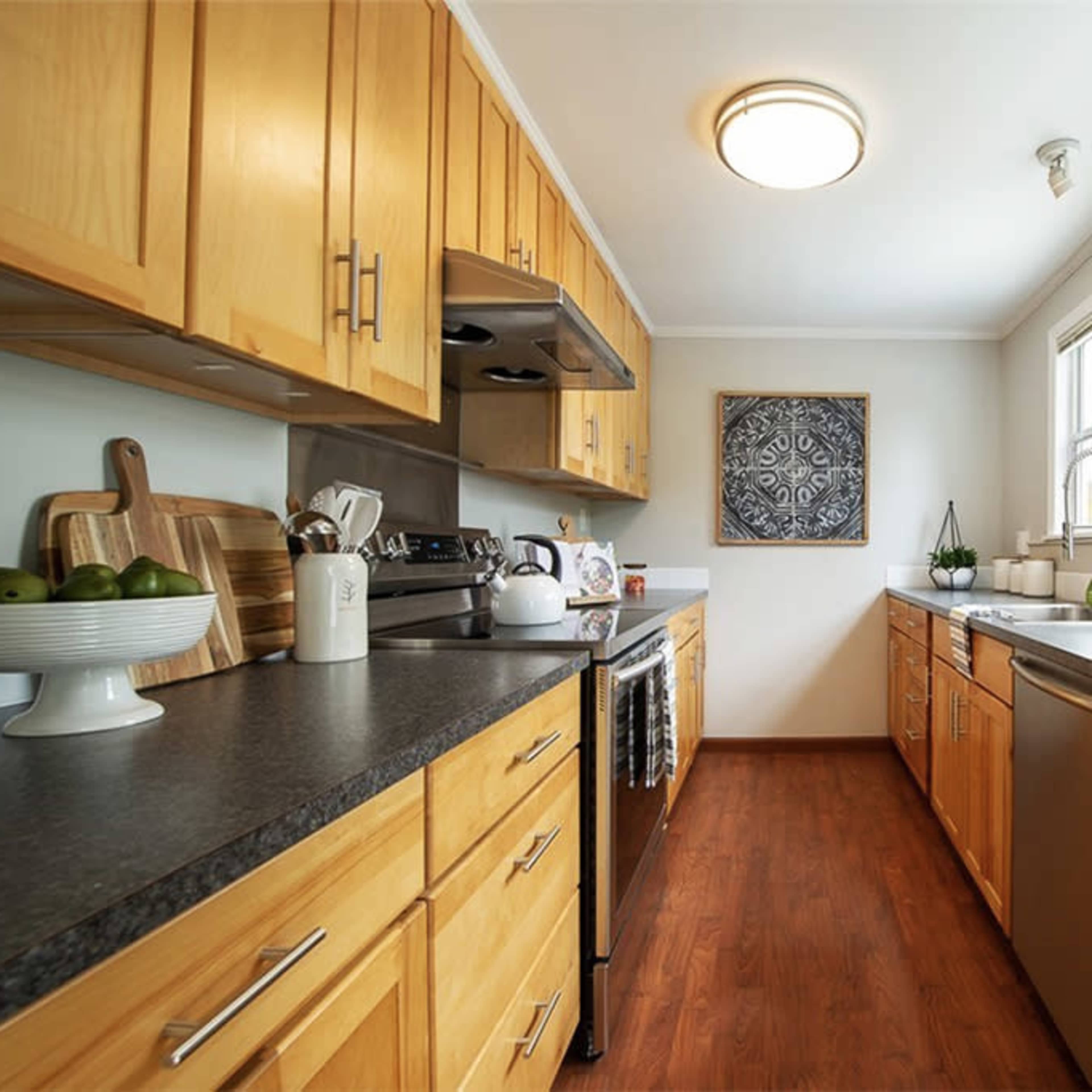 A modern kitchen with wooden cabinets, stainless steel appliances, and a countertop featuring a bowl of green apples.