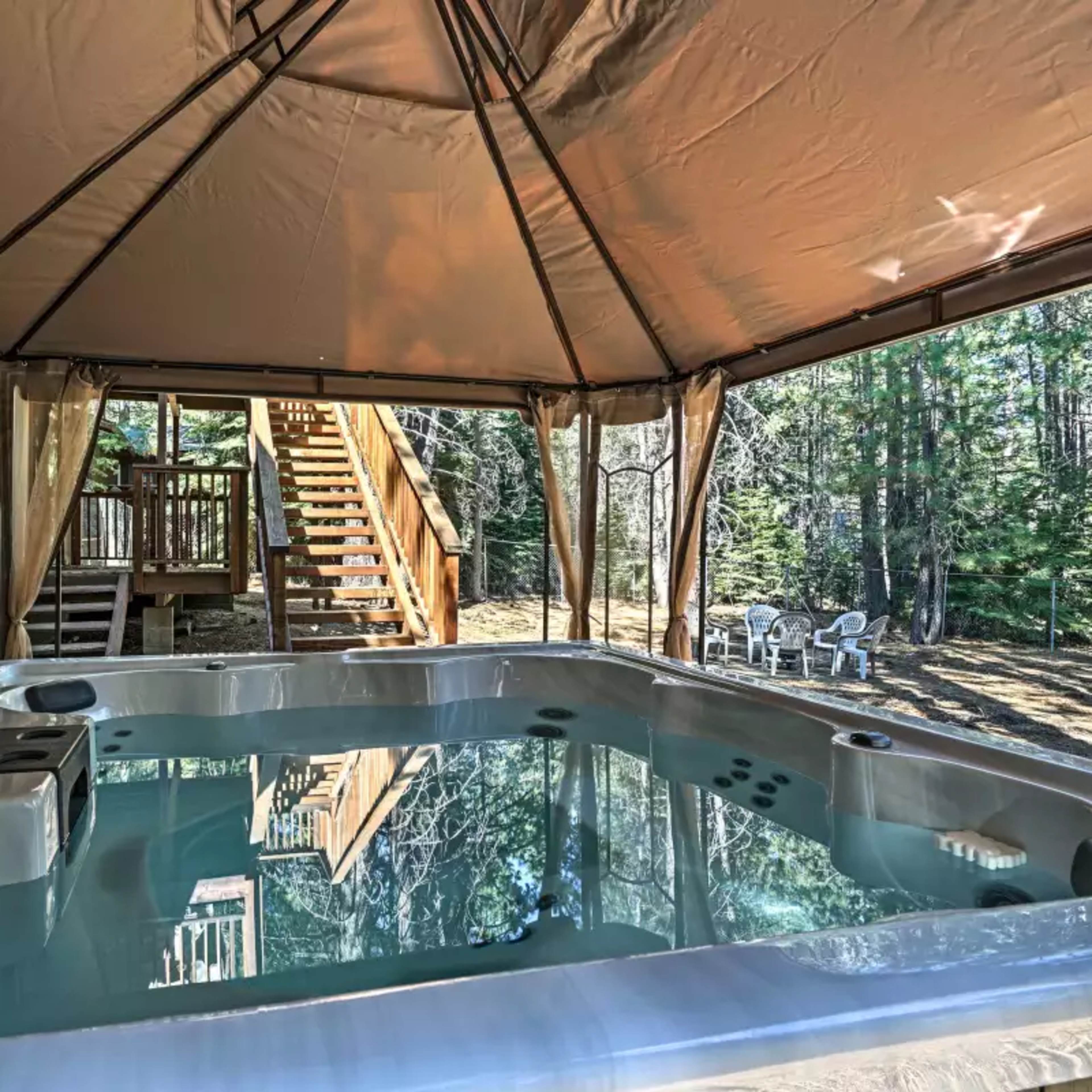 A hot tub under a canopy with a wooden staircase visible in the background leading to an outdoor area with white chairs.