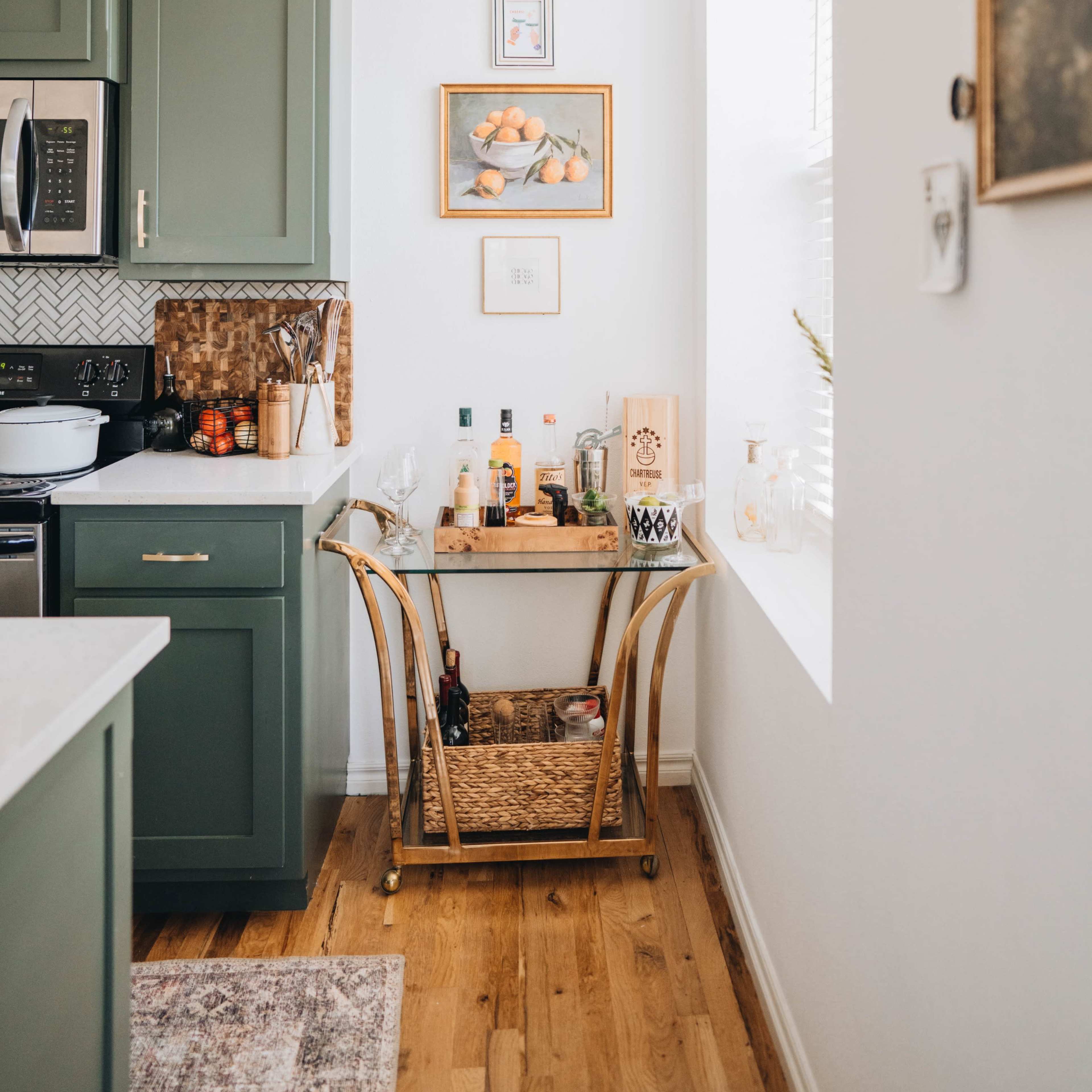 A small kitchen corner features a cart with various bottles and a framed picture on the wall above it.