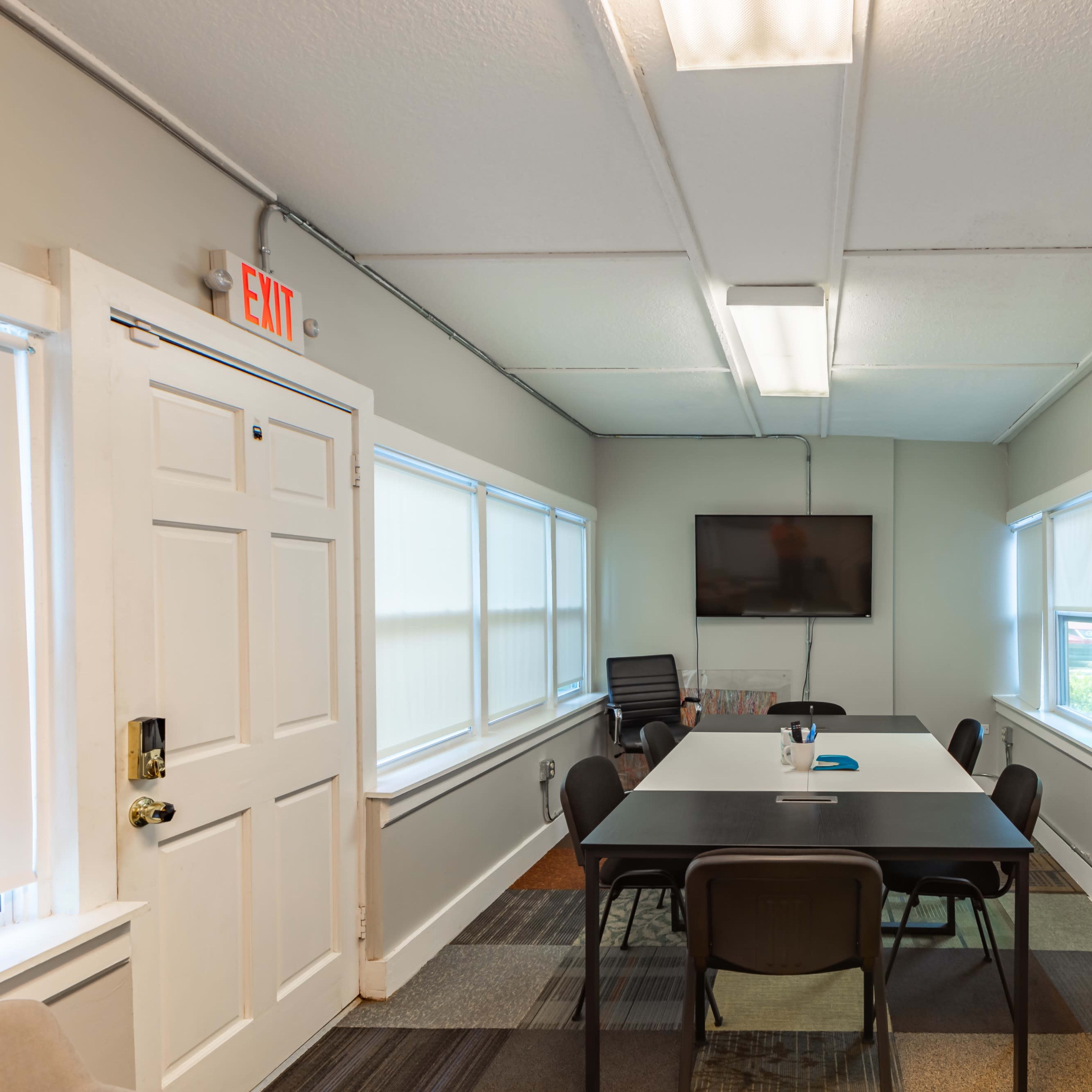 A conference room featuring a long table with chairs, a television mounted on the wall, and a whiteboard.