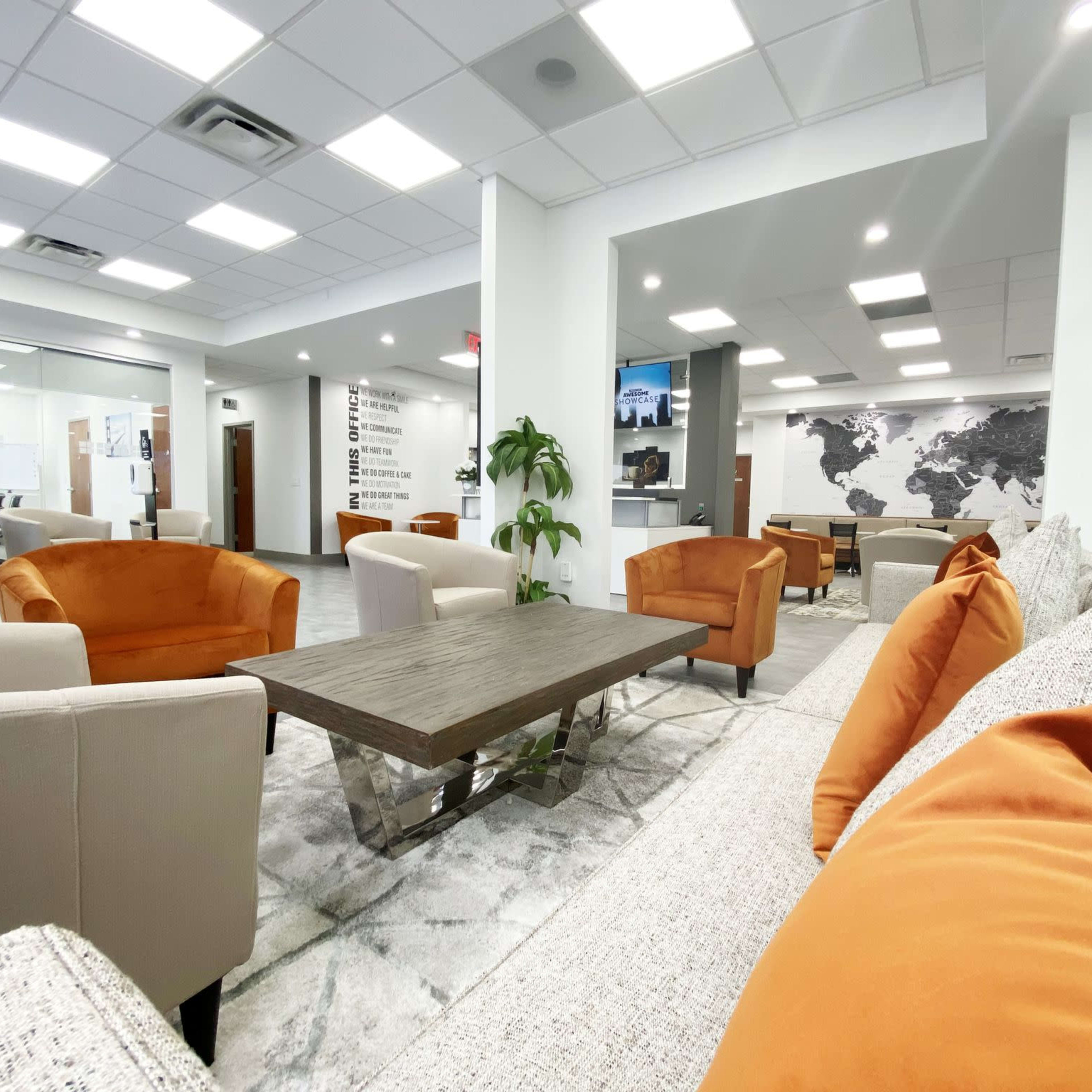 A modern office lounge area with orange armchairs and a large coffee table on a light rug, framed by a wall featuring a world map.