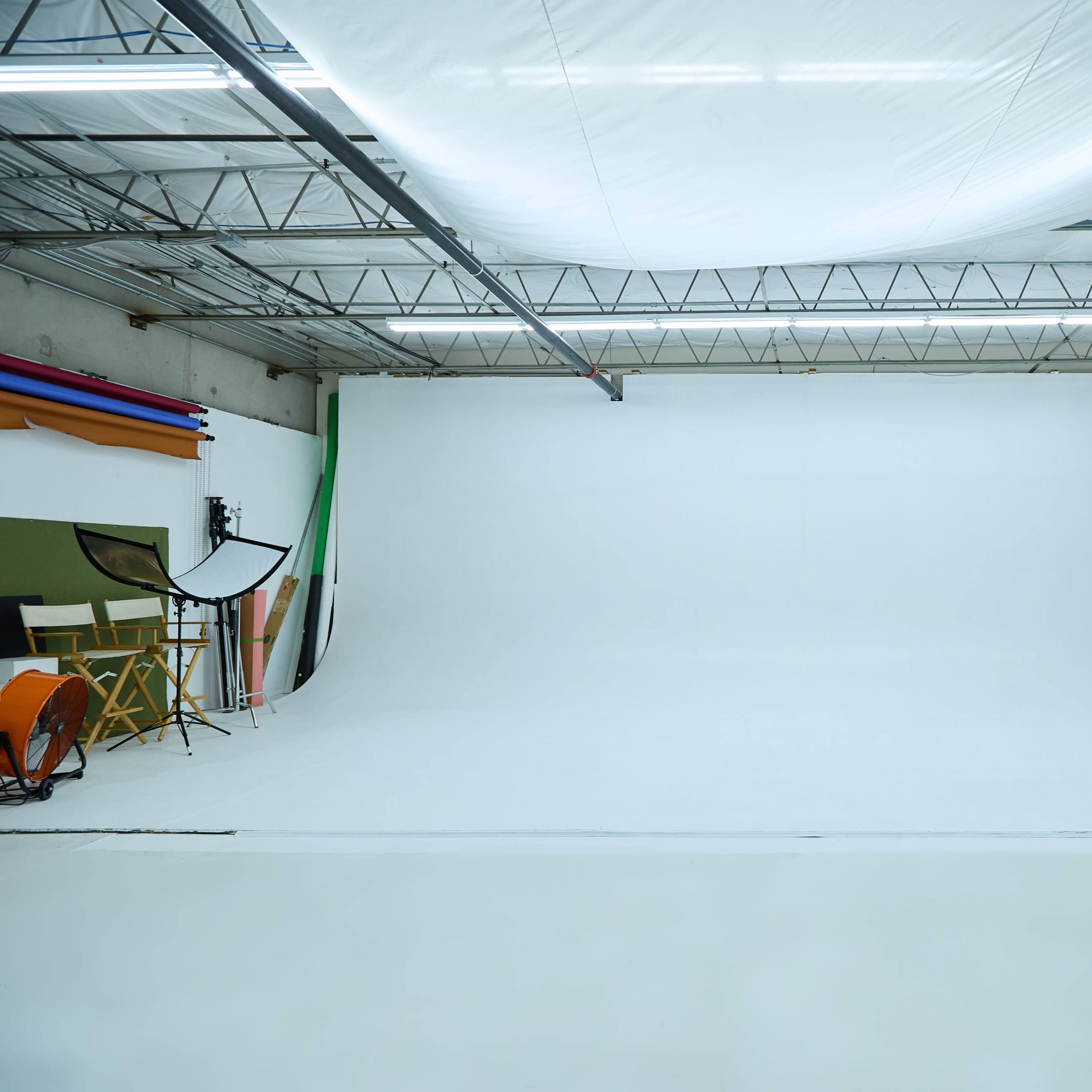 A spacious photography studio with a large white backdrop and various colorful backdrop rolls along the walls.