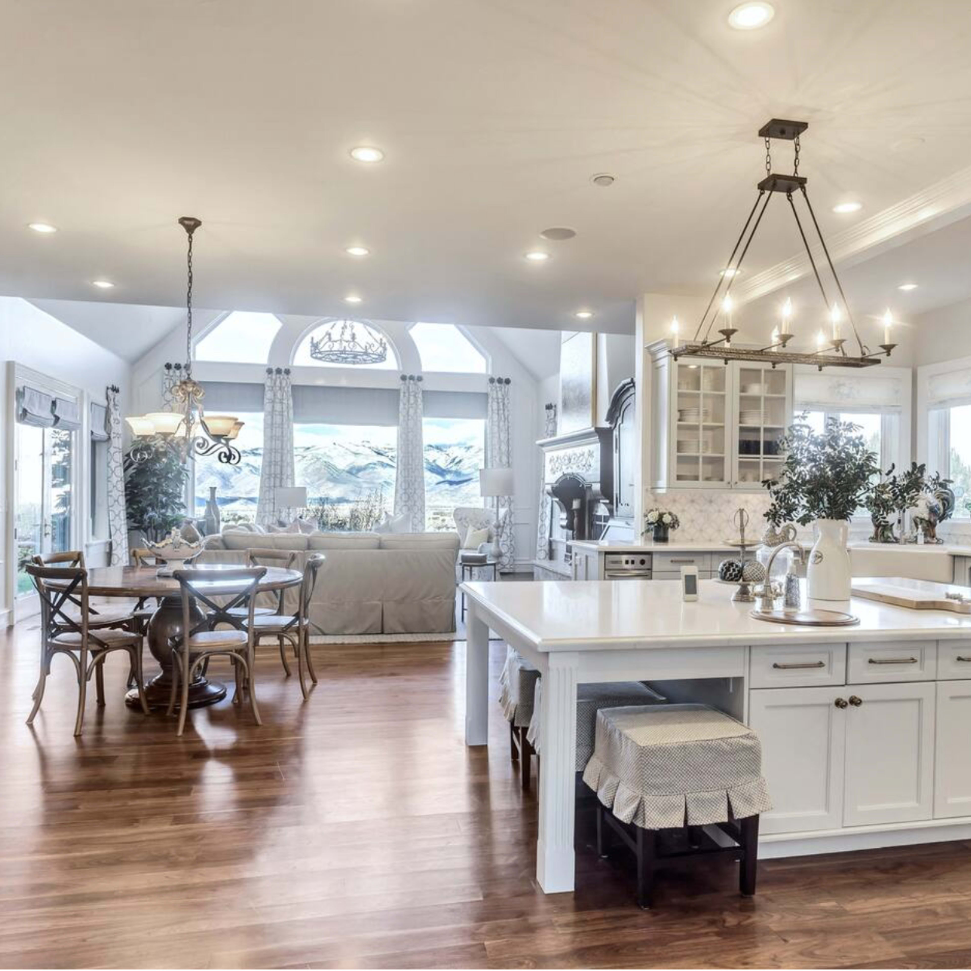 A bright and spacious kitchen features a large island, white cabinetry, and a dining area with a table and chairs, all set against a backdrop of large windows.